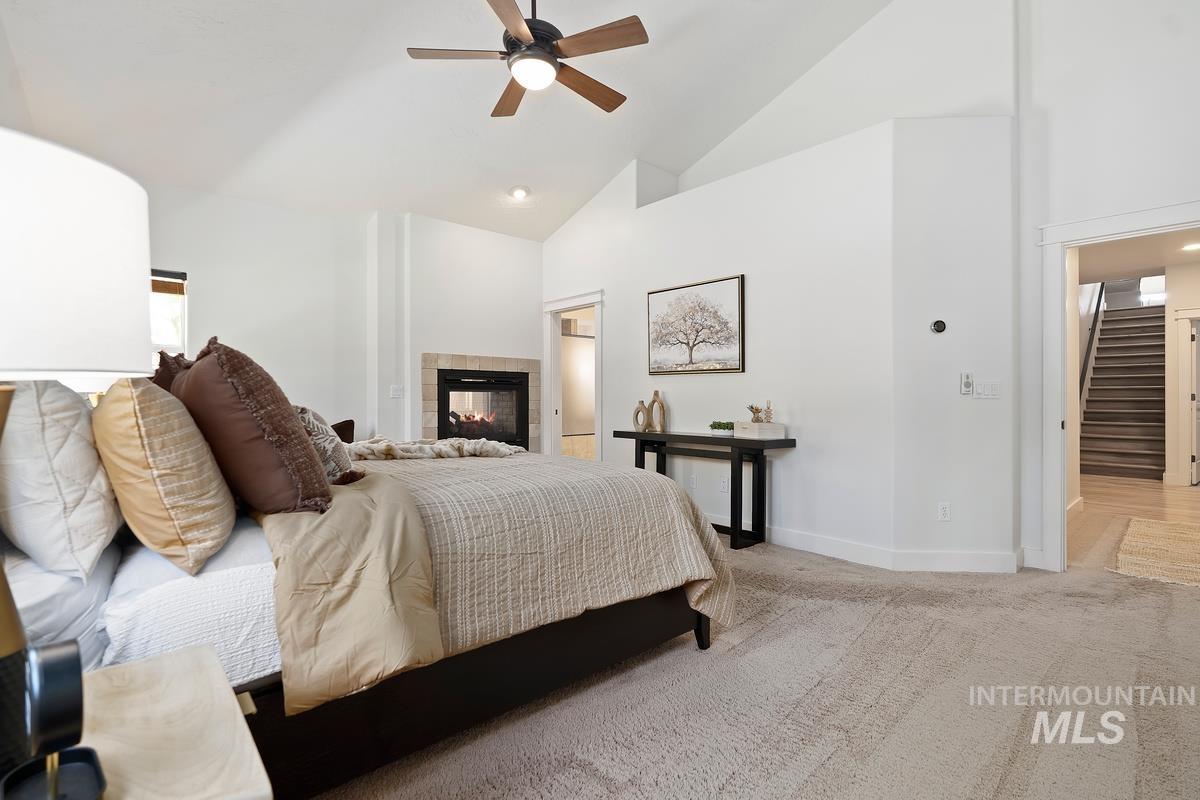 Bedroom featuring high vaulted ceiling, light colored carpet, a tile fireplace, and ceiling fan