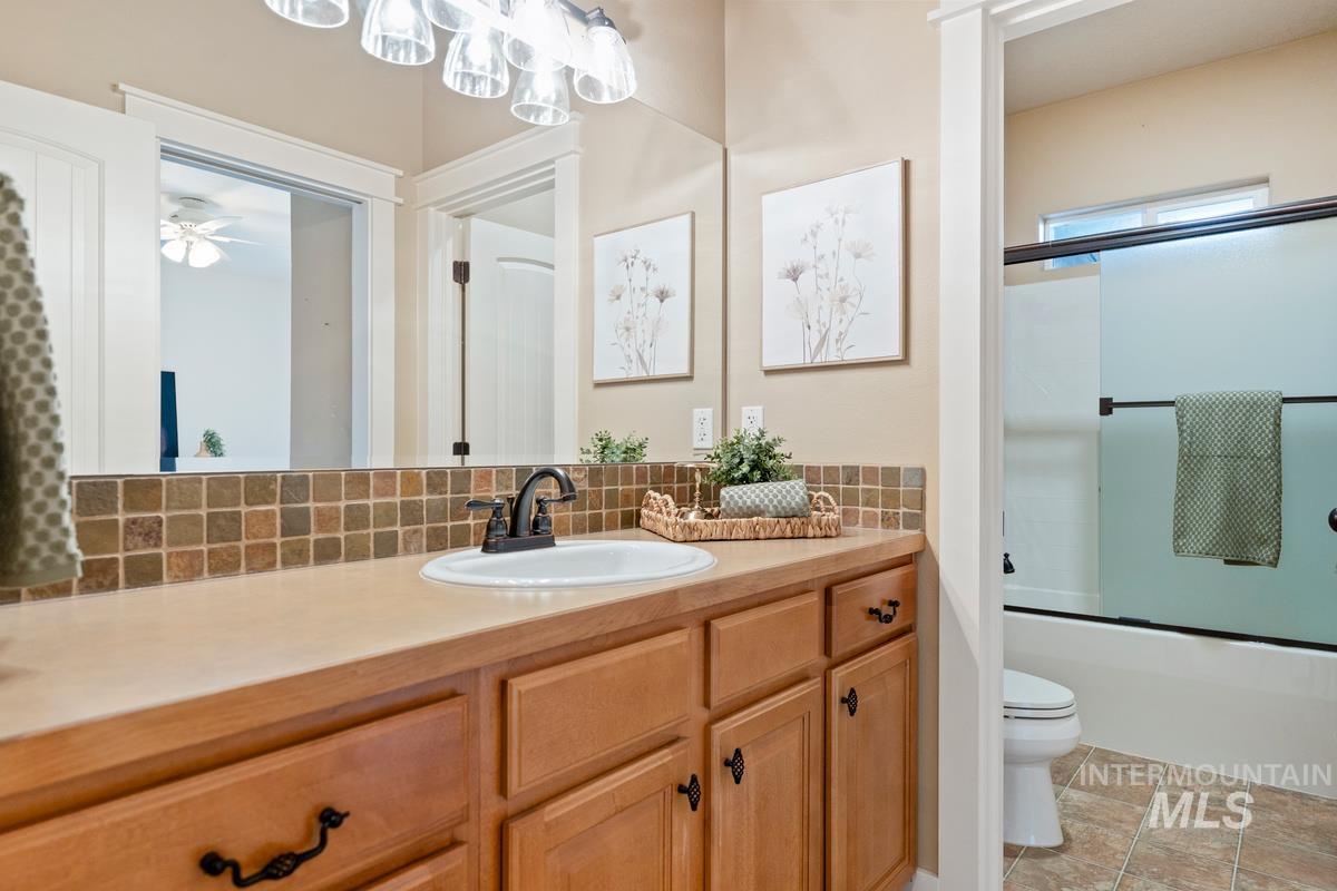 Bathroom featuring vanity, decorative backsplash, and bath / shower combo with glass door
