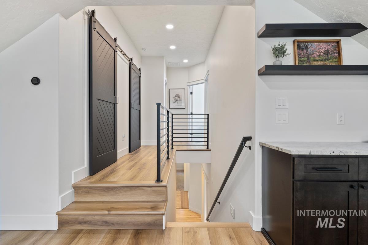 Stairs with a barn door, recessed lighting, and wood finished floors