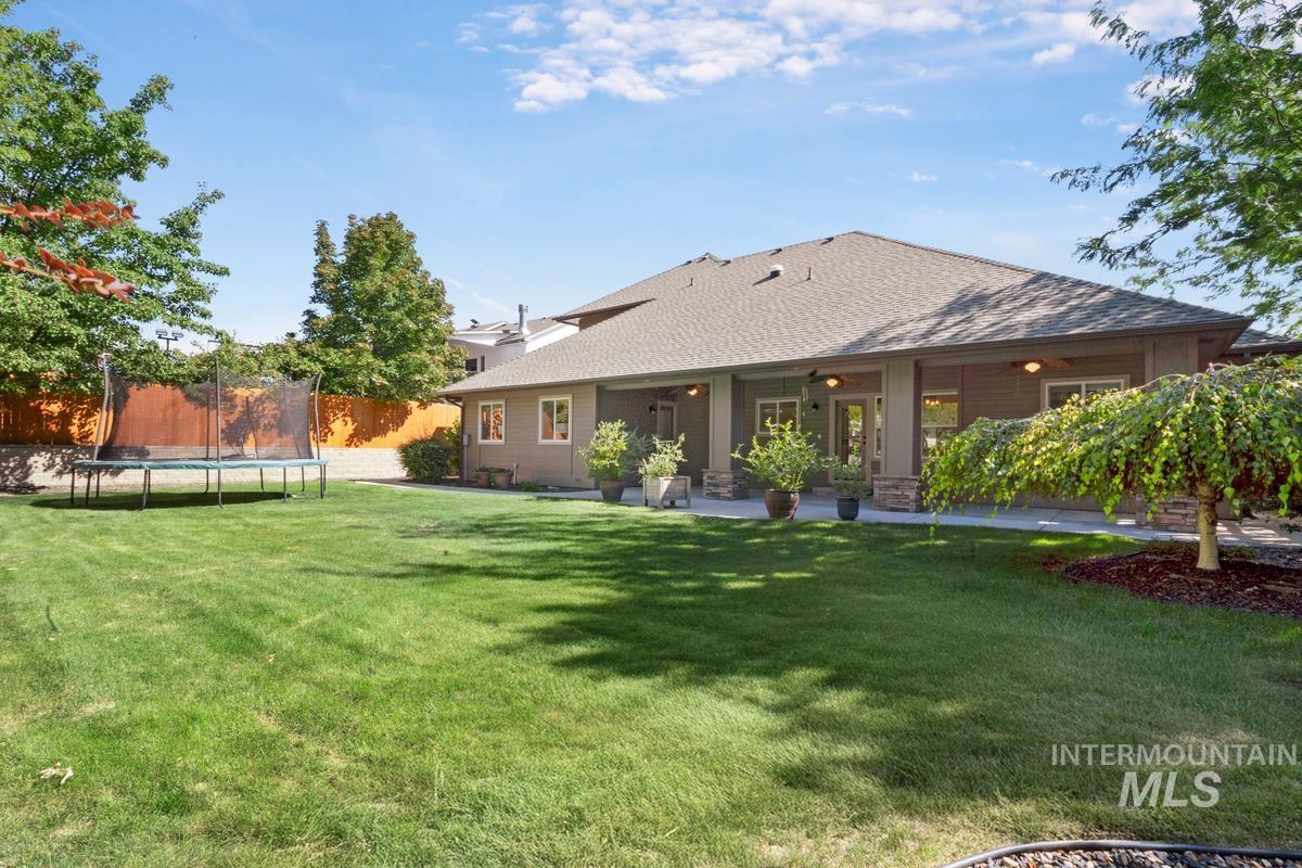 Back of property with a trampoline, a shingled roof, and a patio area