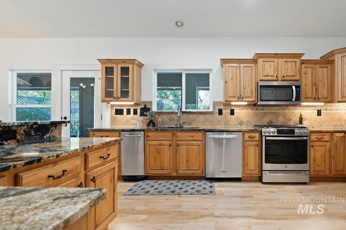 Kitchen featuring dark stone counters, appliances with stainless steel finishes, tasteful backsplash, light wood finished floors, and recessed lighting