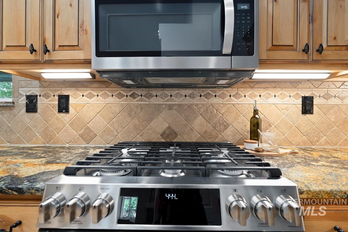 Kitchen view of stainless steel appliances, dark stone countertops, backsplash, and brown cabinetry