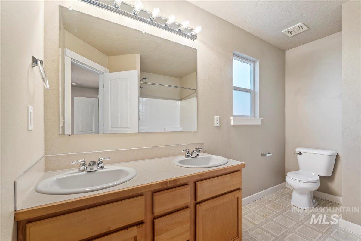 Full bath featuring double vanity, a shower, and a textured ceiling