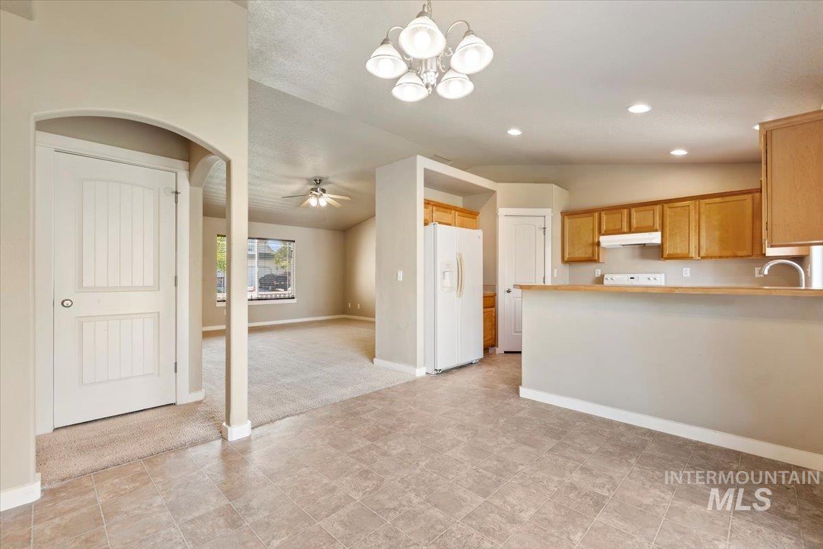 Kitchen featuring vaulted ceiling, pendant lighting, white fridge with ice dispenser, a chandelier, and light colored carpet
