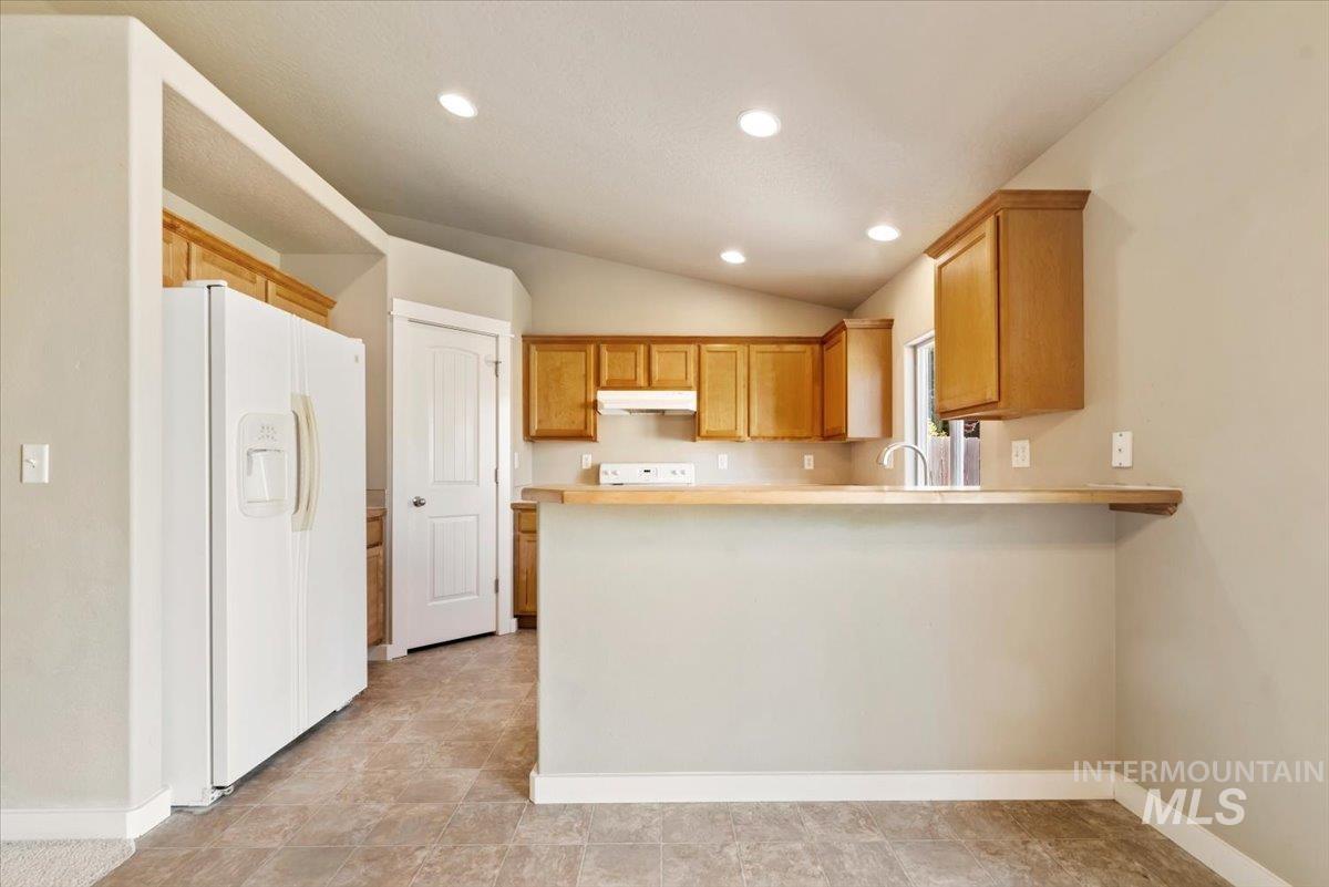 Kitchen with white appliances, vaulted ceiling, light countertops, recessed lighting, and a peninsula