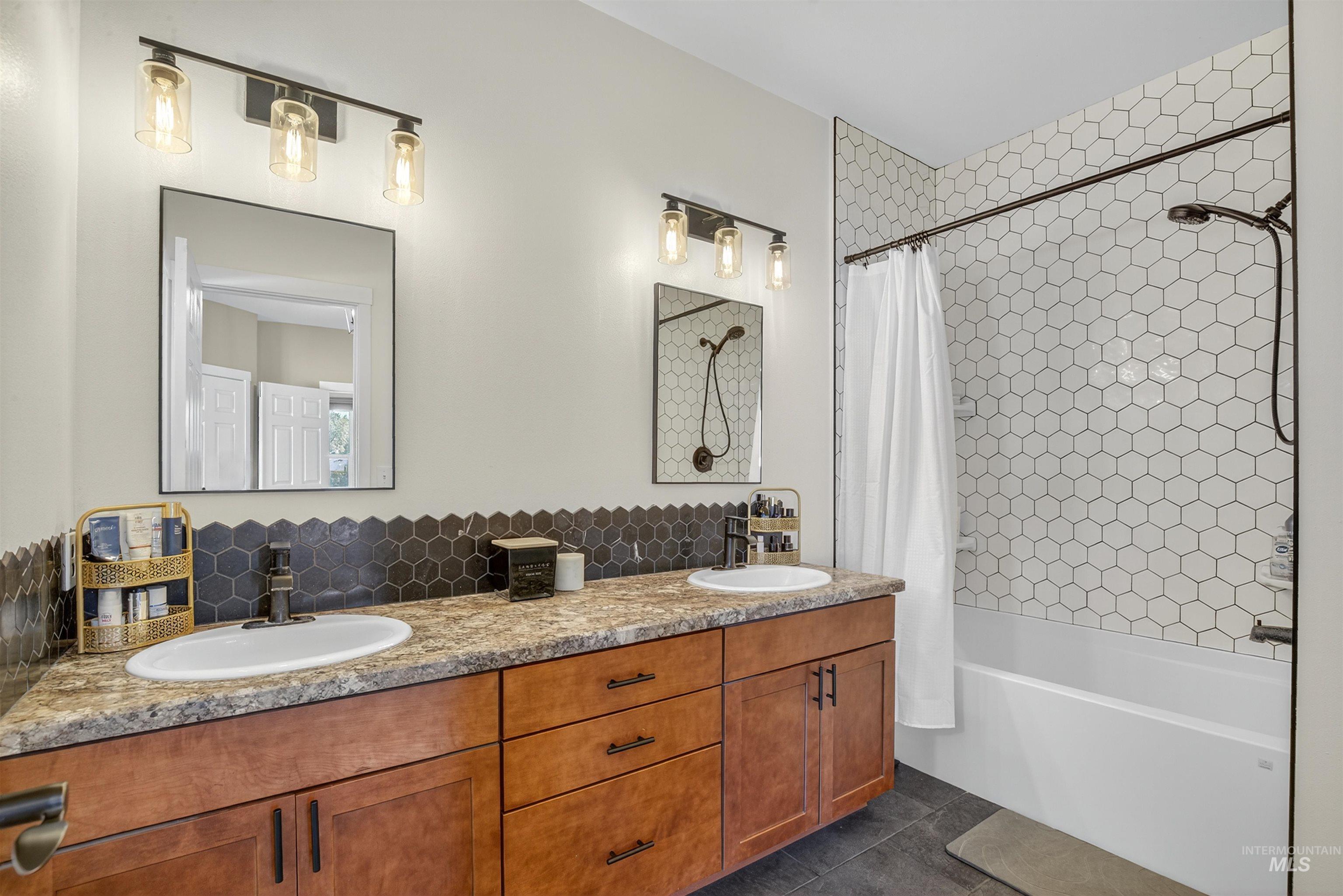 Full bathroom featuring shower / bath combo with shower curtain, dark tile patterned floors, and double vanity