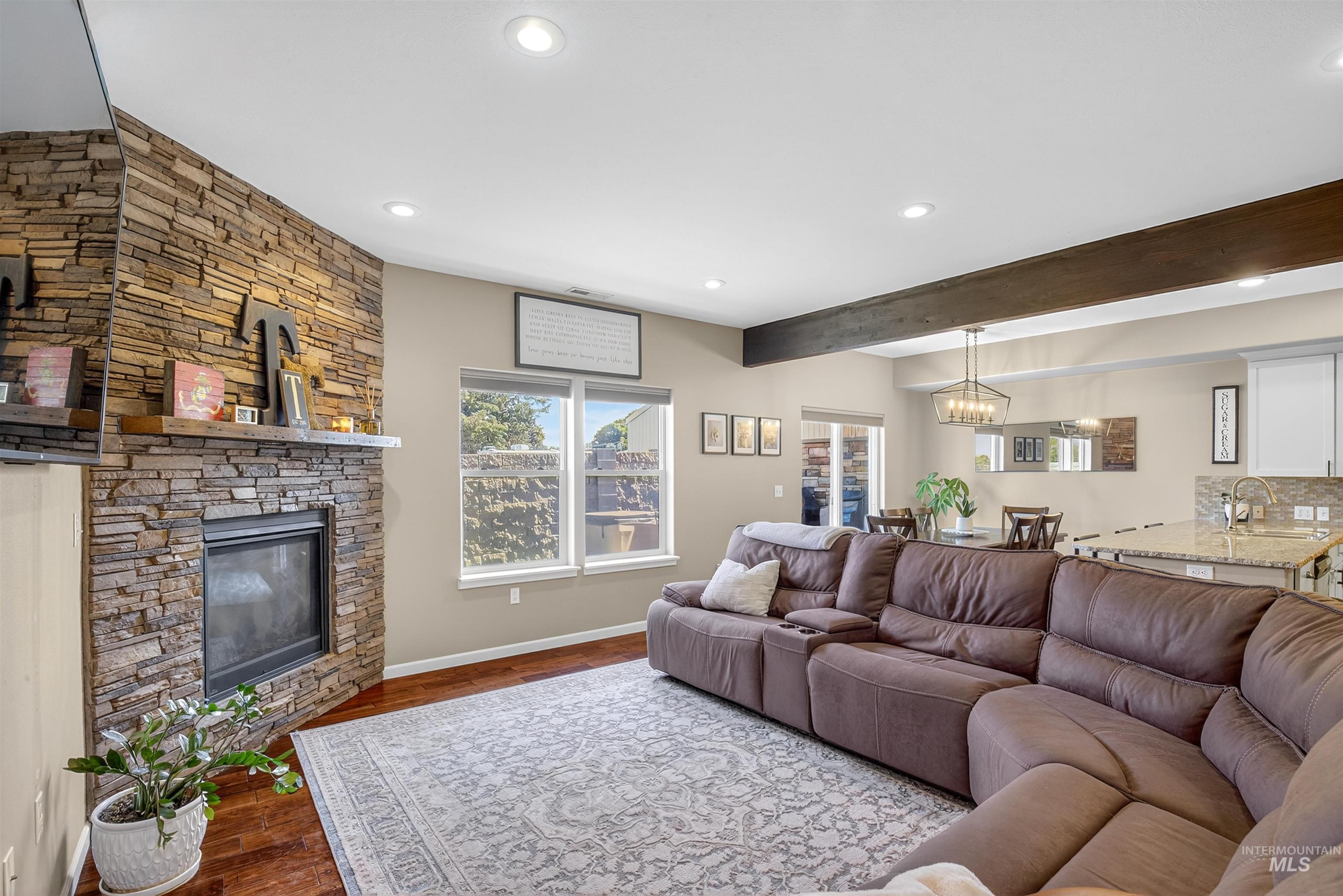 Living area featuring a stone fireplace, recessed lighting, dark wood-type flooring, and beamed ceiling