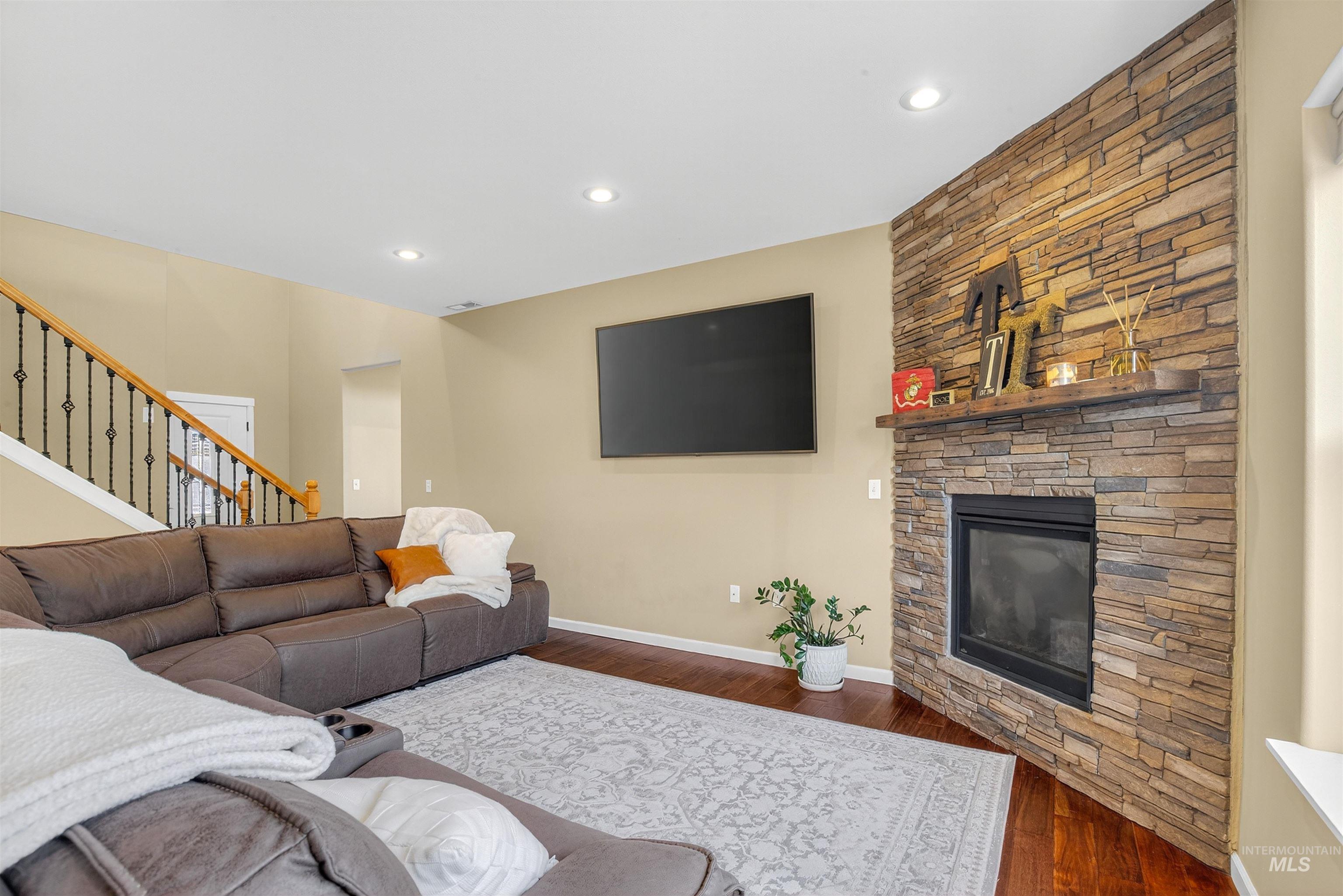 Living room with a stone fireplace, wood finished floors, recessed lighting, and stairs