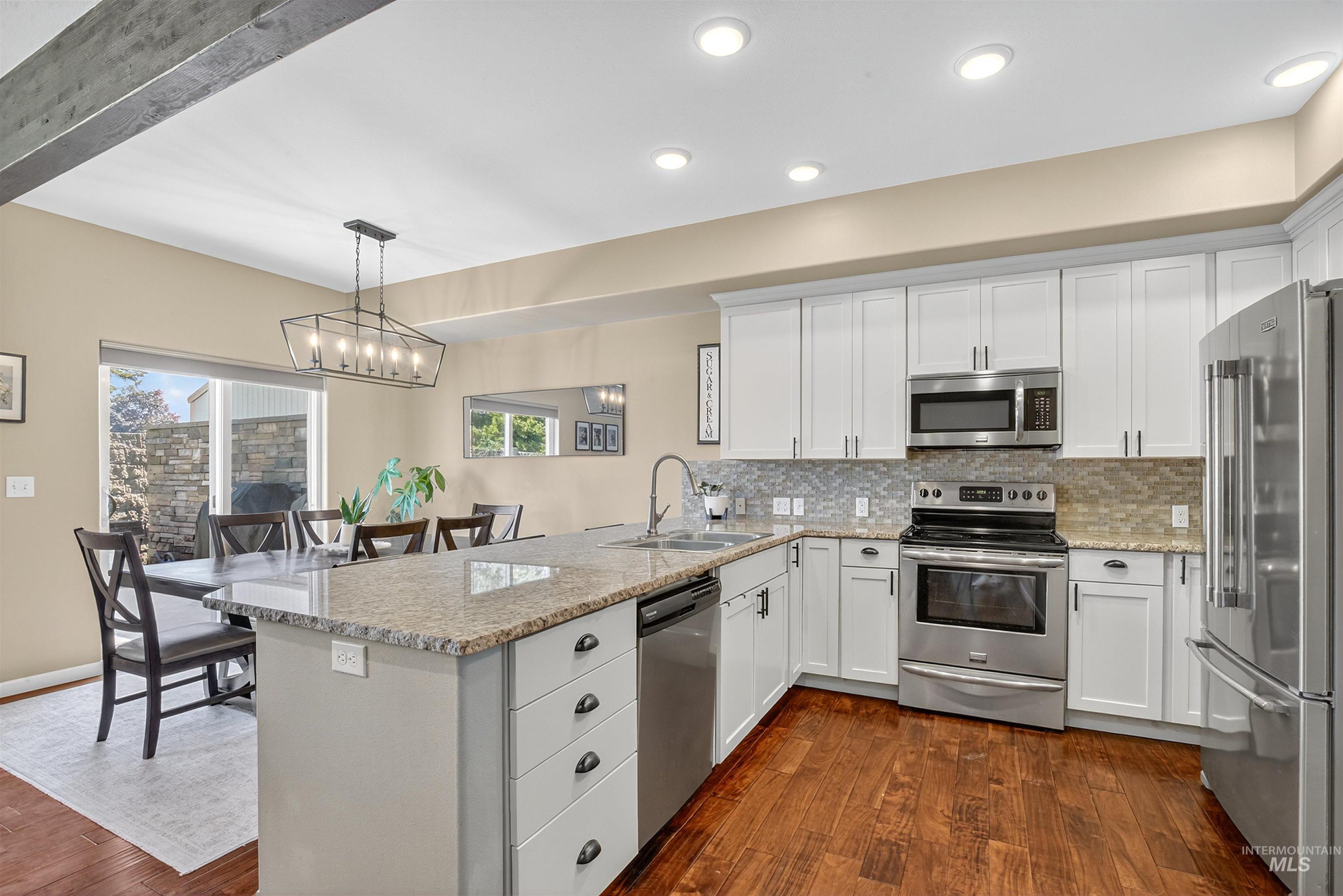 Kitchen featuring appliances with stainless steel finishes, white cabinets, a peninsula, dark wood-type flooring, and decorative light fixtures