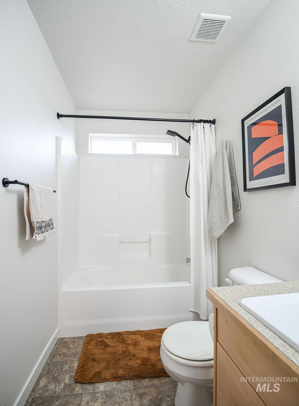 Bathroom featuring shower / bath combo, vanity, a textured ceiling, and dark stone finish flooring