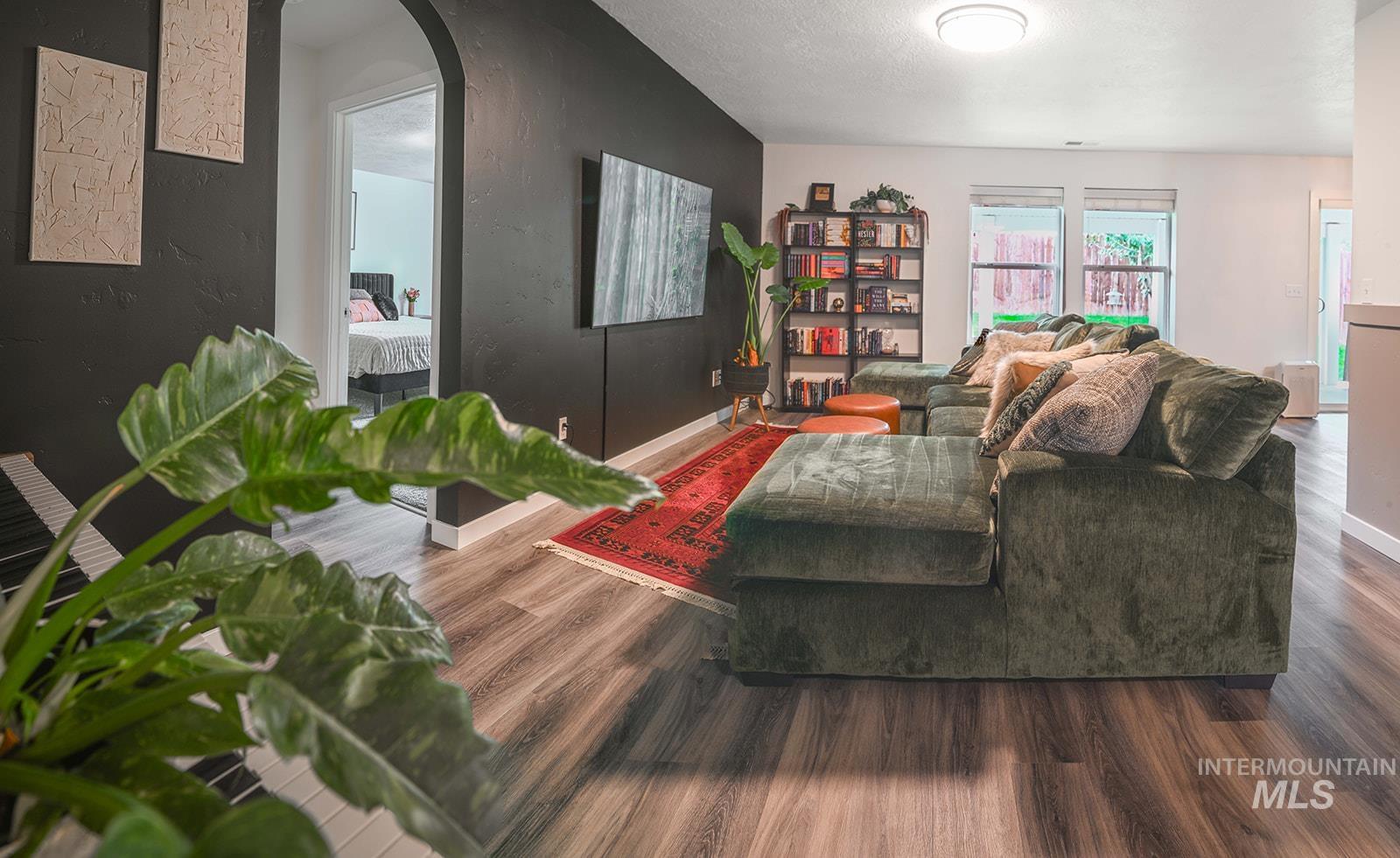 Living room featuring arched walkways, wood finished floors, a textured ceiling, and a textured wall