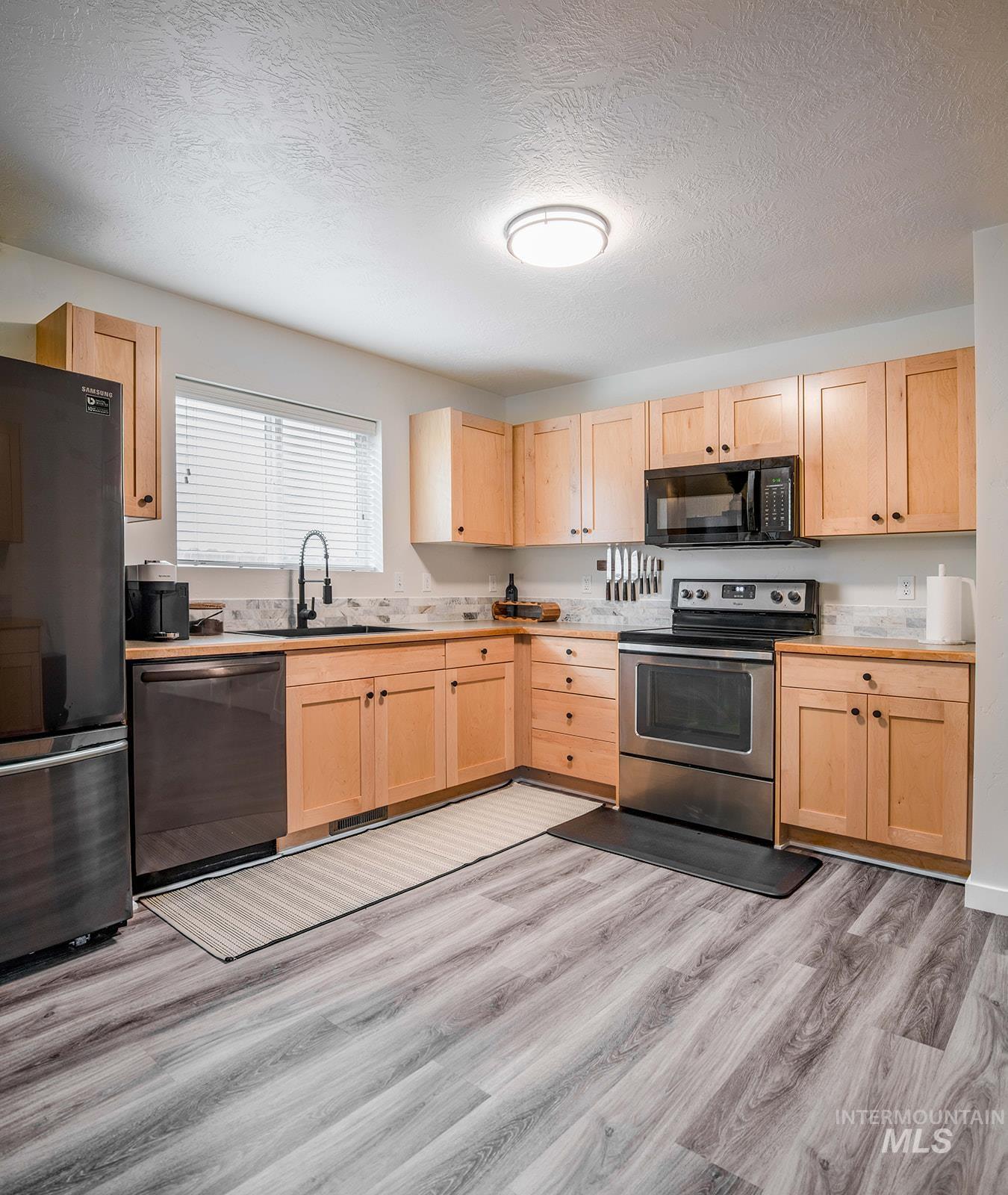 Kitchen featuring light brown cabinets, black appliances, a textured ceiling, light countertops, and light wood-style floors
