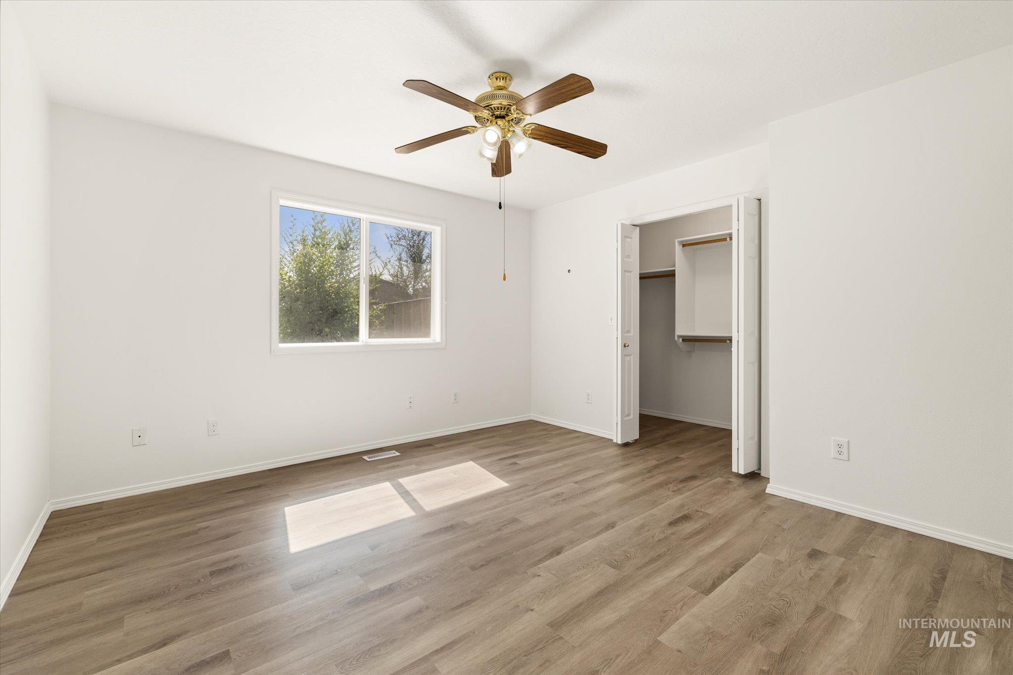 Unfurnished bedroom featuring a spacious closet, light wood-style flooring, and ceiling fan