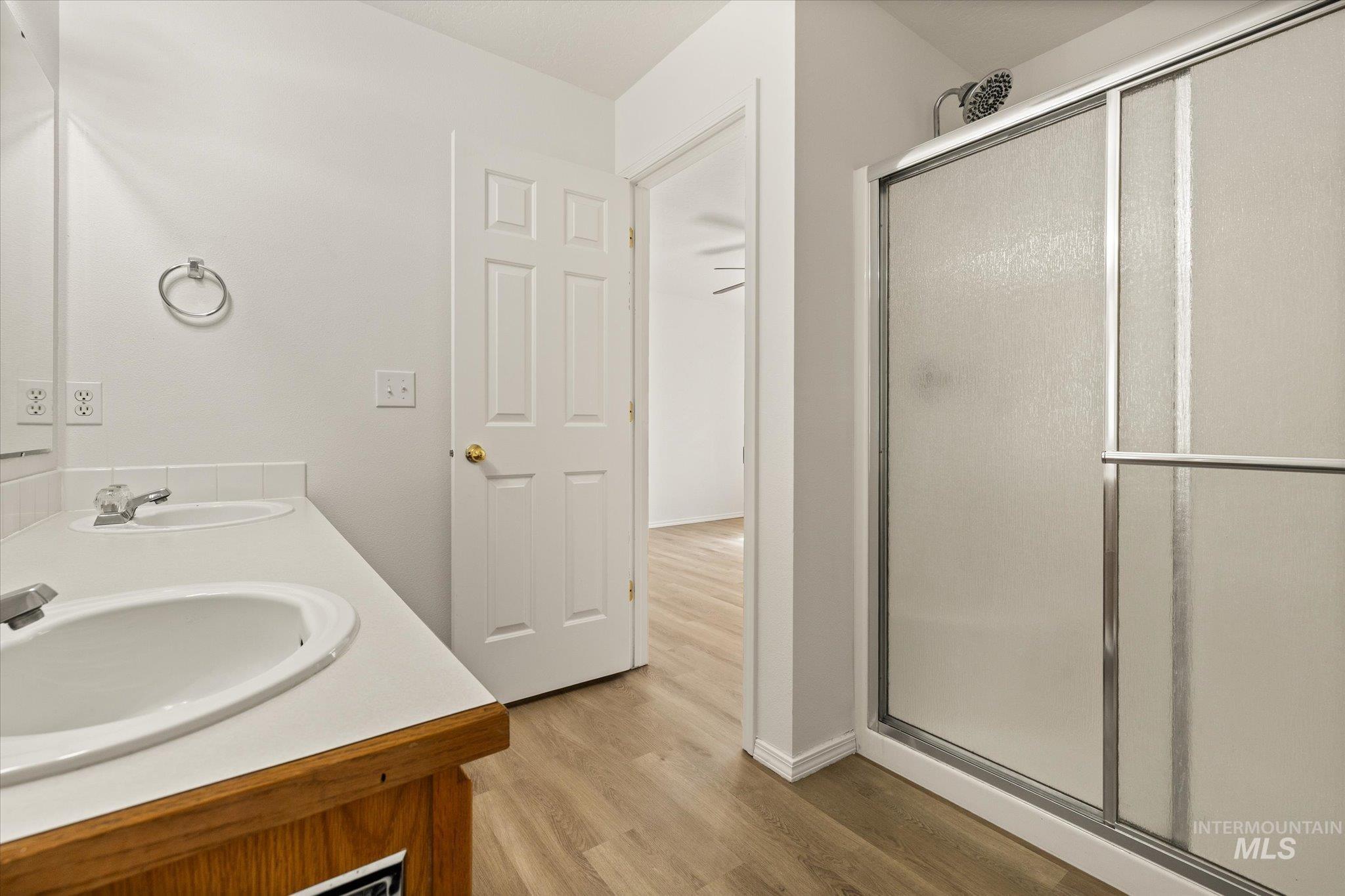 Full bathroom featuring a stall shower, light wood finished floors, and double vanity