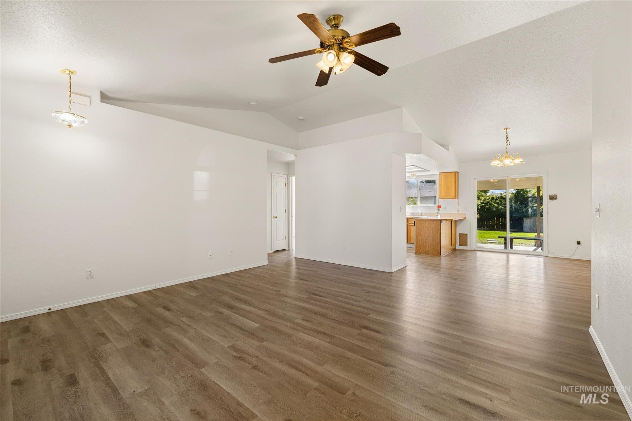 Unfurnished living room with a chandelier, lofted ceiling, ceiling fan, and dark wood-style flooring
