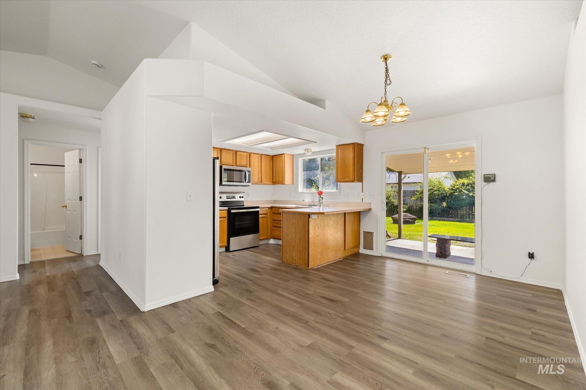 Kitchen featuring lofted ceiling, light countertops, stainless steel appliances, dark wood-style flooring, and open floor plan