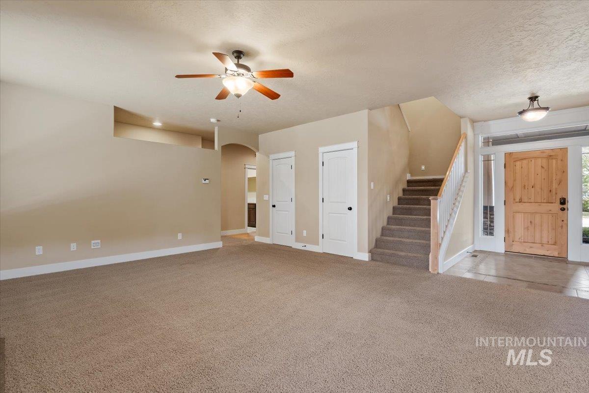 Unfurnished living room featuring light carpet, stairway, arched walkways, a textured ceiling, and ceiling fan