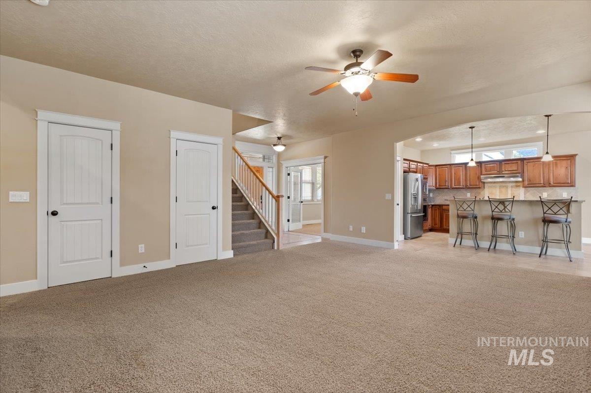Unfurnished living room featuring a textured ceiling, light colored carpet, stairs, and ceiling fan