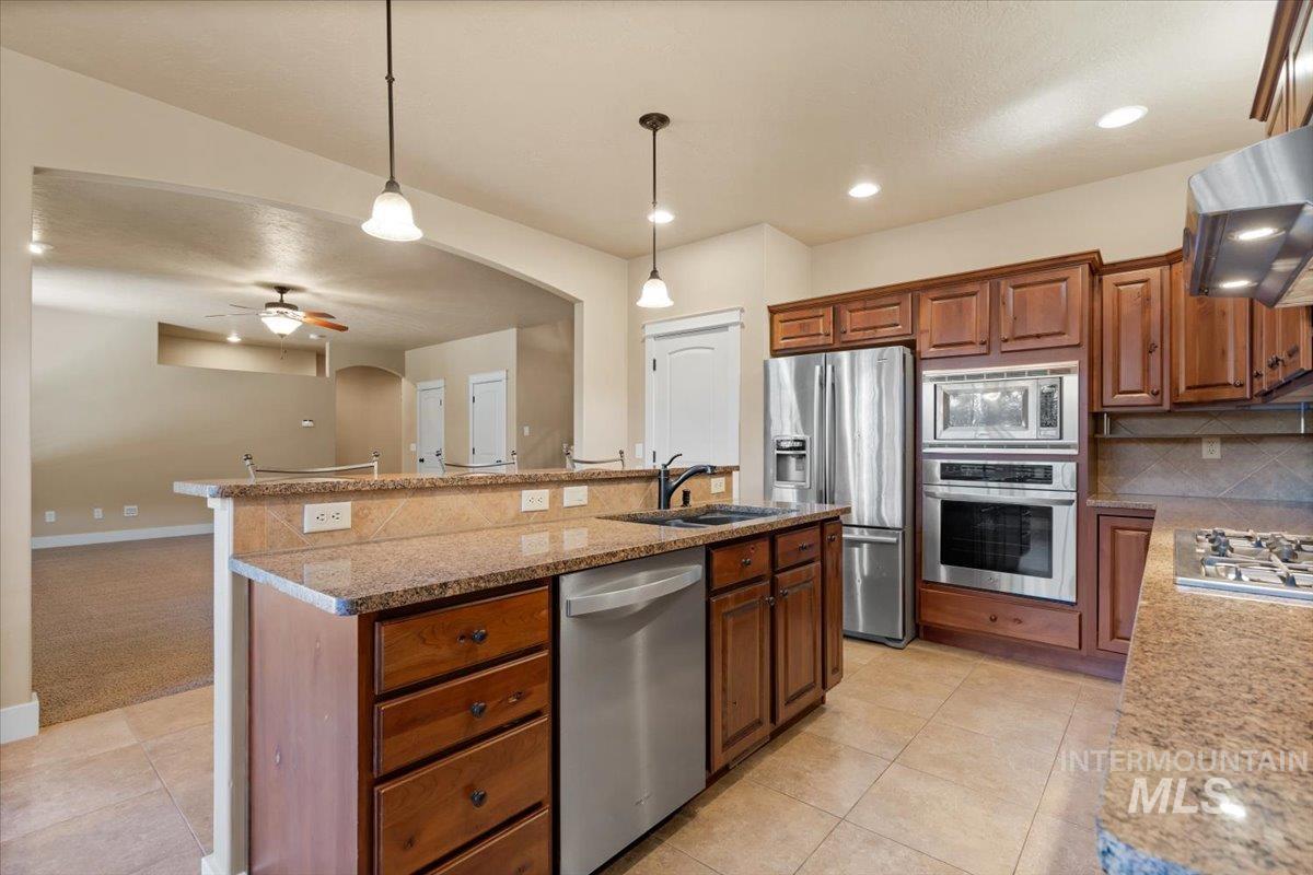 Kitchen with arched walkways, pendant lighting, decorative backsplash, appliances with stainless steel finishes, and a kitchen island with sink