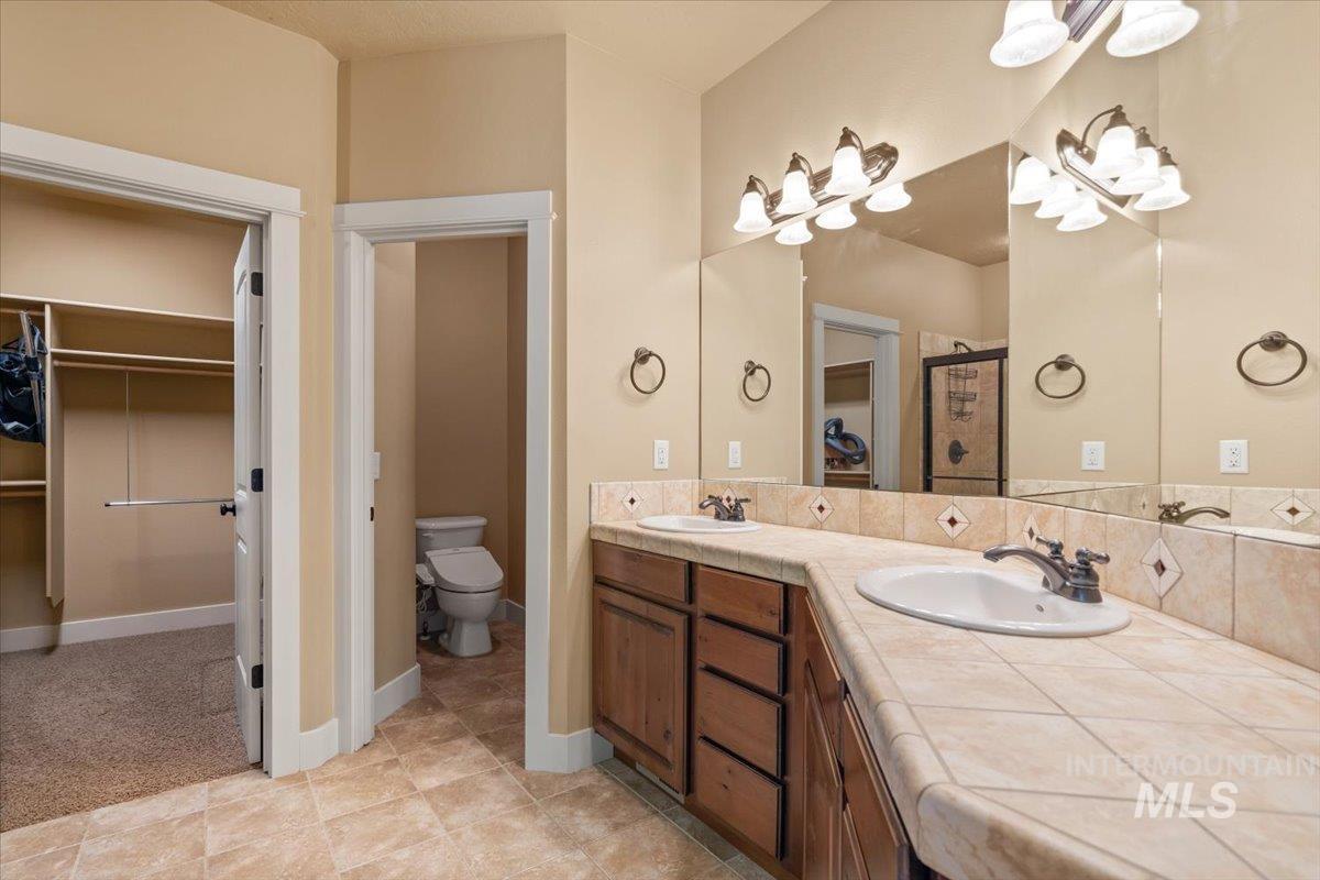 Bathroom with a walk in closet, double vanity, a shower stall, and light tile patterned floors