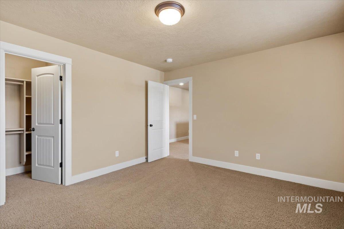 Unfurnished bedroom with light carpet, a textured ceiling, and a walk in closet