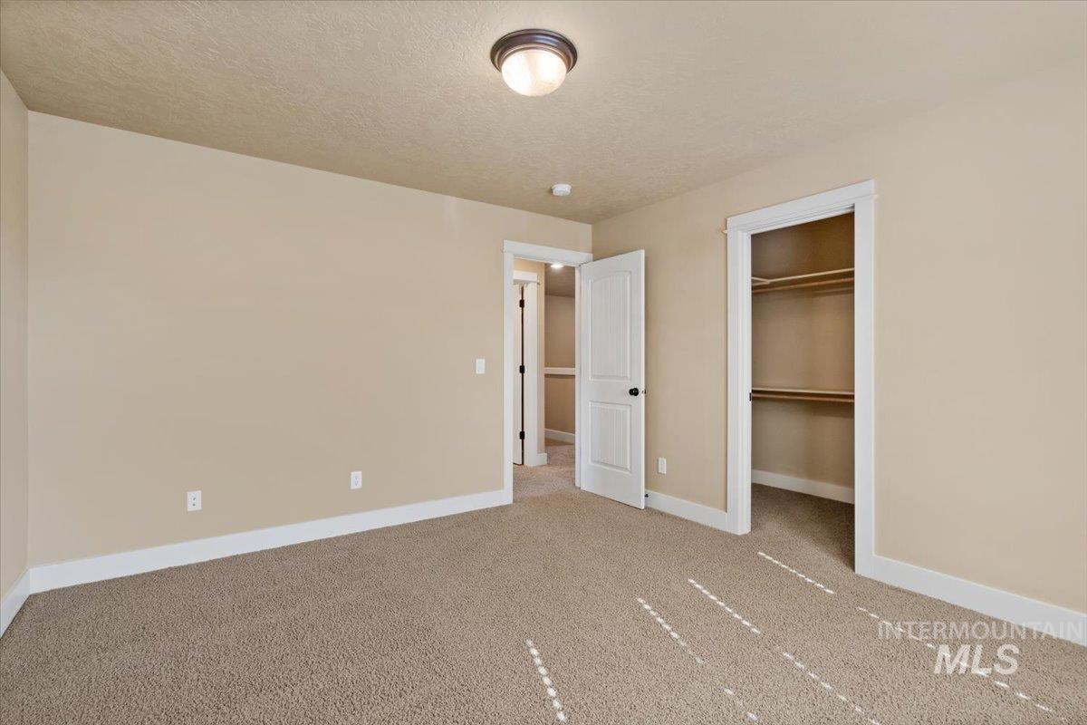 Unfurnished bedroom featuring light colored carpet, a textured ceiling, and a spacious closet