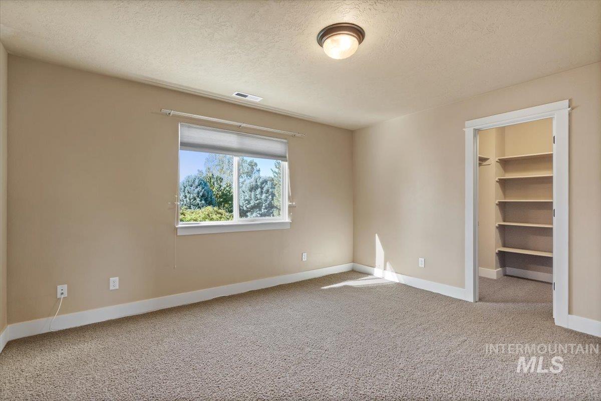 Unfurnished bedroom featuring a walk in closet, light colored carpet, and a textured ceiling
