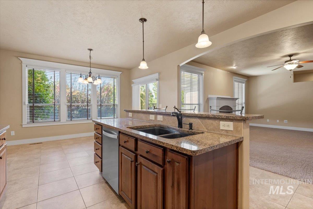 Kitchen featuring a textured ceiling, hanging light fixtures, a center island with sink, light stone counters, and stainless steel dishwasher