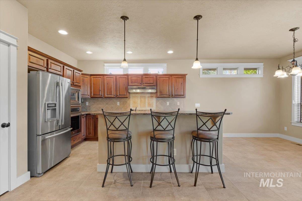 Kitchen featuring tasteful backsplash, stainless steel appliances, pendant lighting, a breakfast bar, and brown cabinets