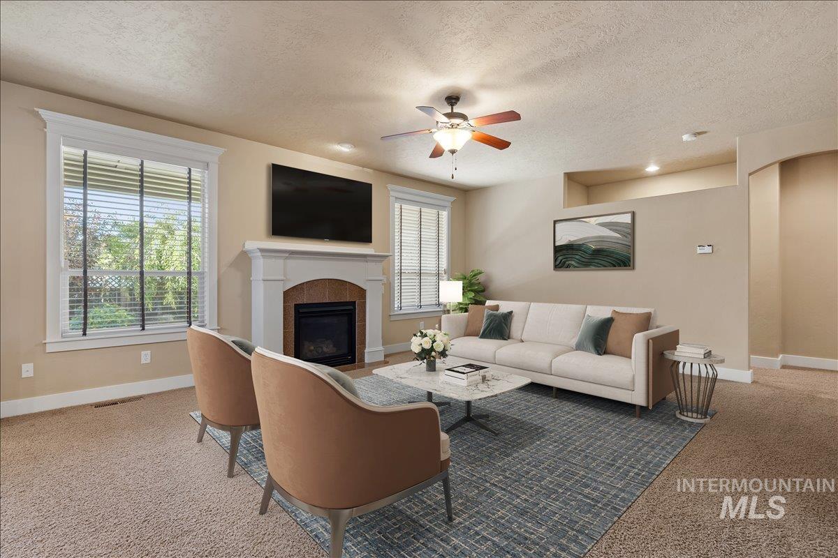 Carpeted living room featuring a textured ceiling, a tiled fireplace, and ceiling fan