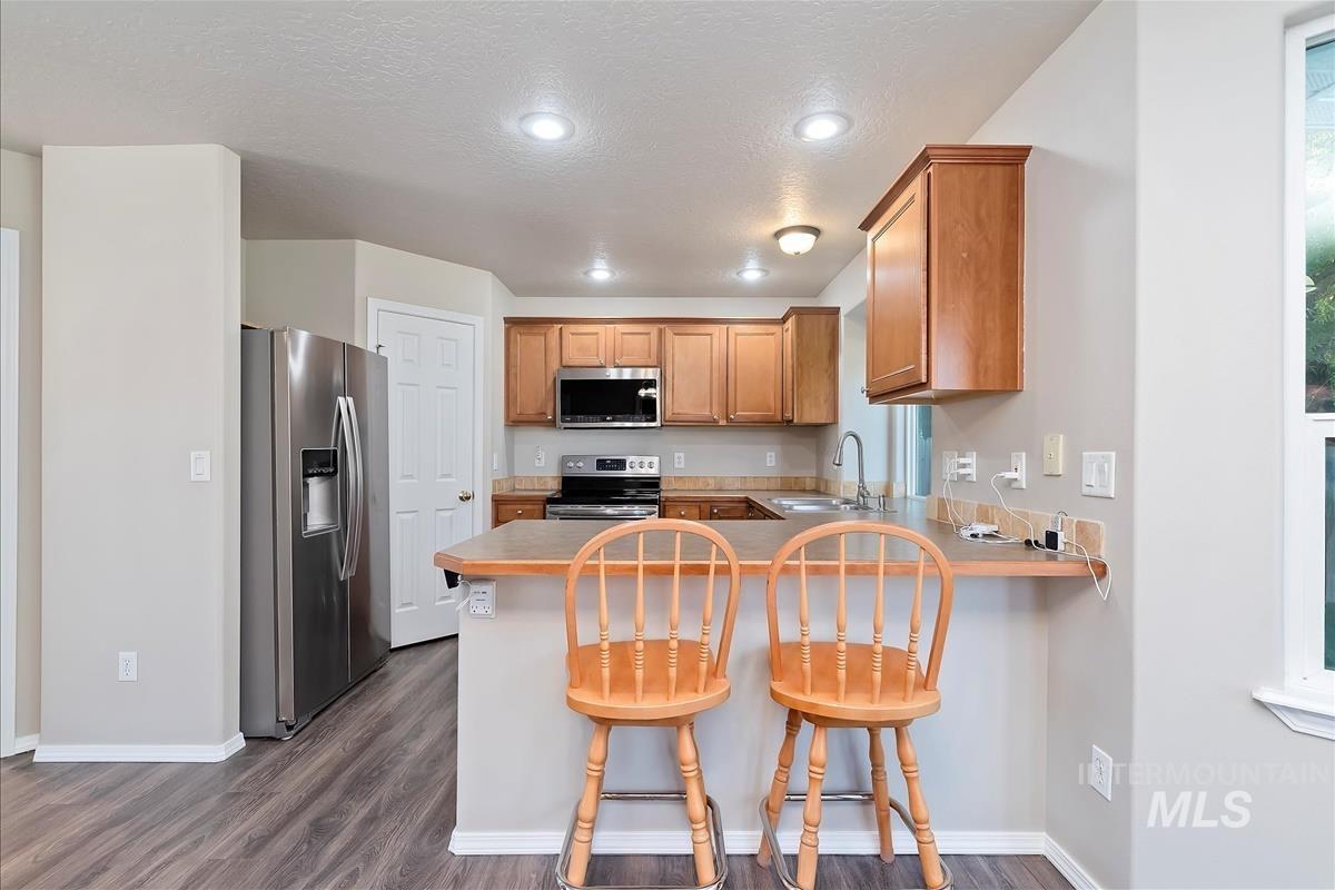 Kitchen with appliances with stainless steel finishes, a kitchen bar, dark wood-style floors, a peninsula, and a textured ceiling
