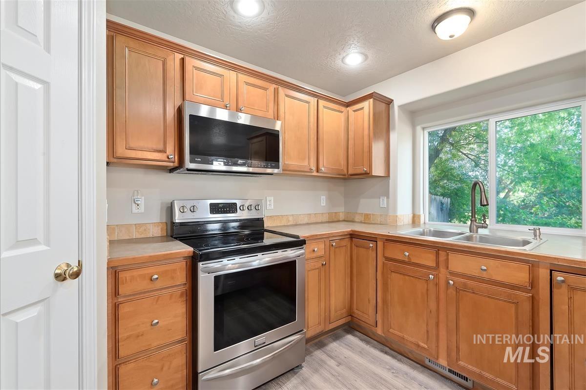 Kitchen with appliances with stainless steel finishes, light countertops, a textured ceiling, light wood-type flooring, and brown cabinets