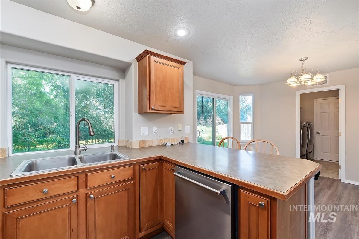 Kitchen with dishwasher, brown cabinets, a textured ceiling, a peninsula, and light countertops