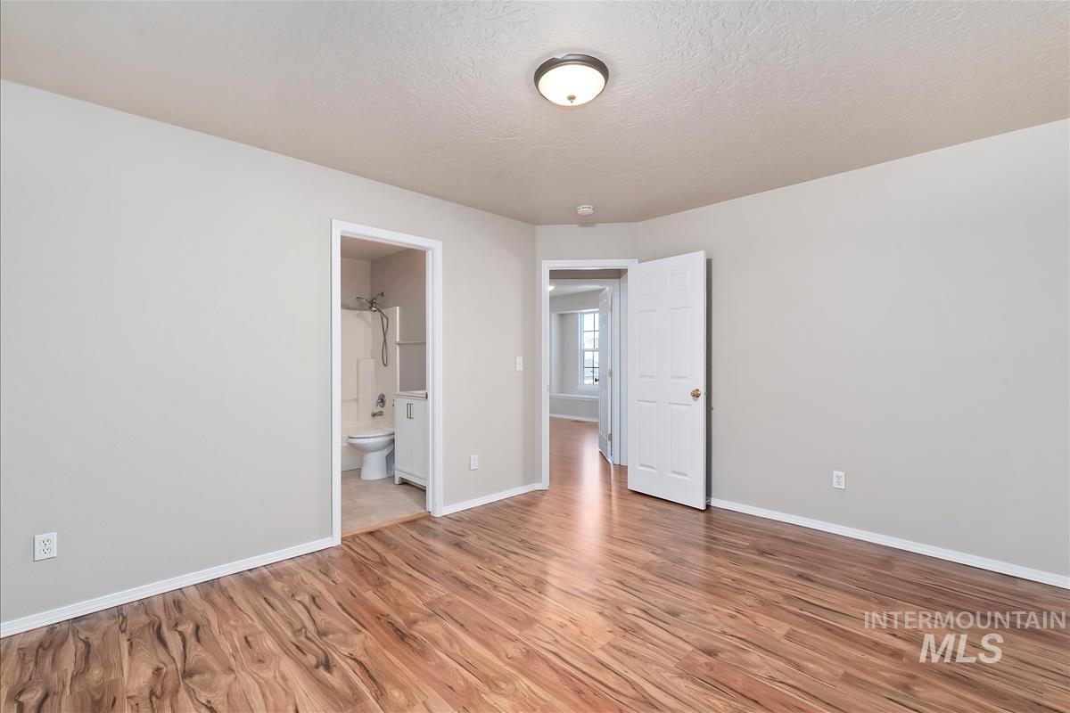 Unfurnished bedroom featuring light wood finished floors, a textured ceiling, and connected bathroom