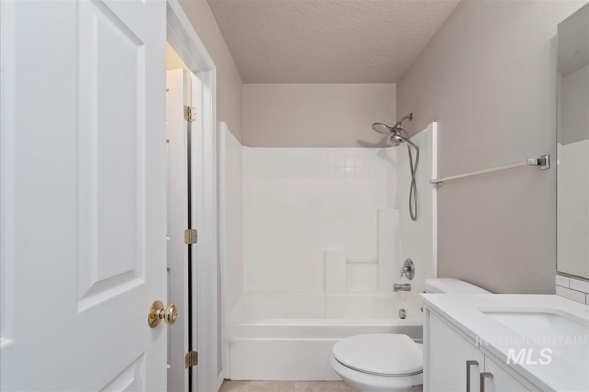 Bathroom featuring vanity, shower / tub combination, a textured ceiling, and light tile patterned floors