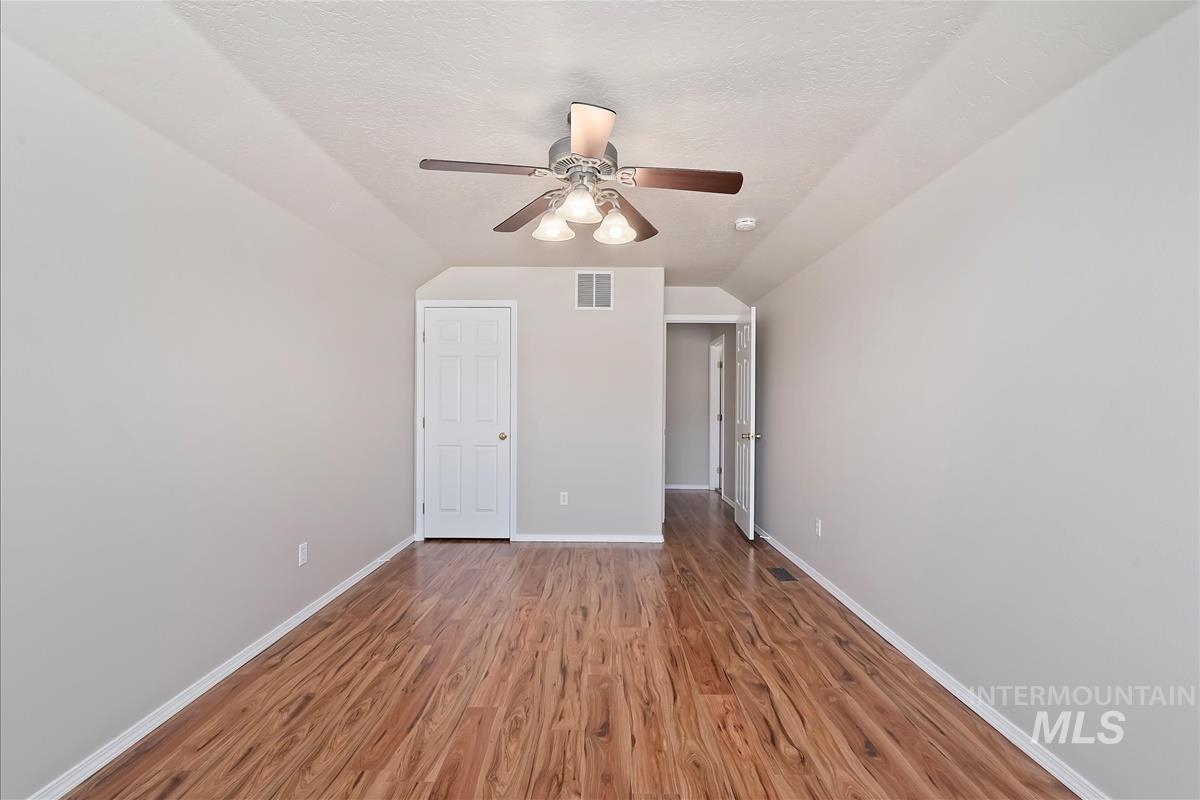 Unfurnished bedroom with wood finished floors, a textured ceiling, ceiling fan, and vaulted ceiling