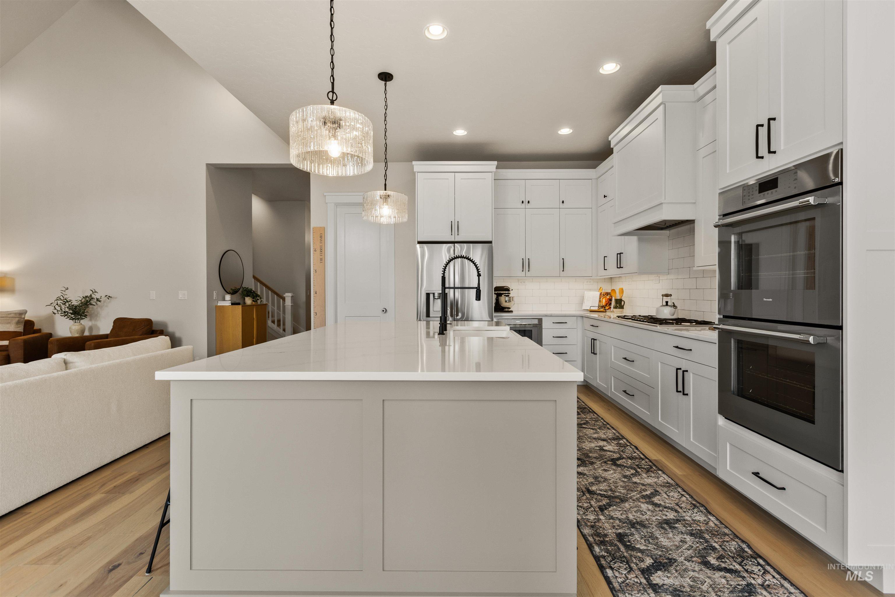 Kitchen featuring appliances with stainless steel finishes, light wood finished floors, backsplash, pendant lighting, and open floor plan