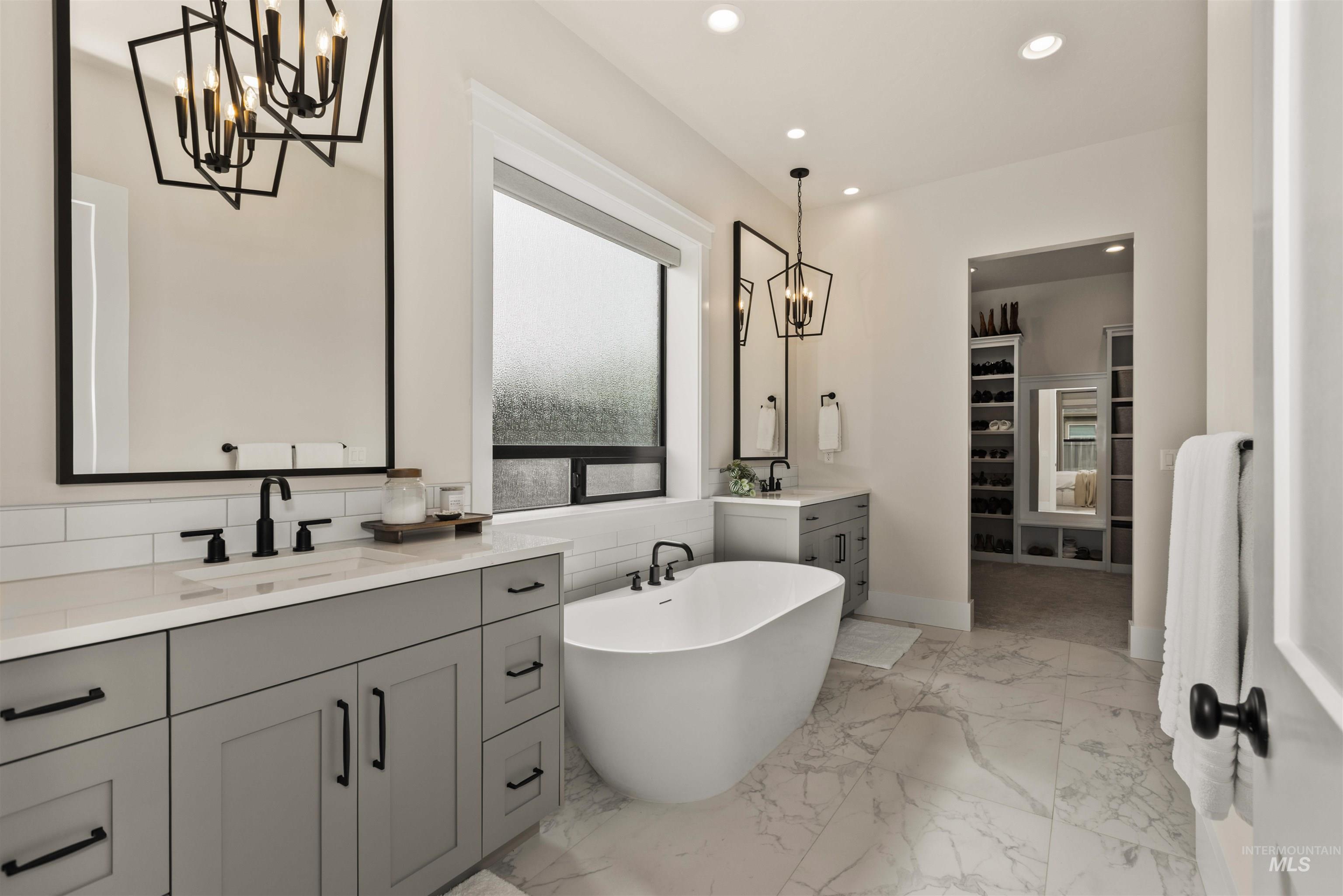 Full bathroom with a chandelier, two vanities, a soaking tub, tasteful backsplash, and recessed lighting