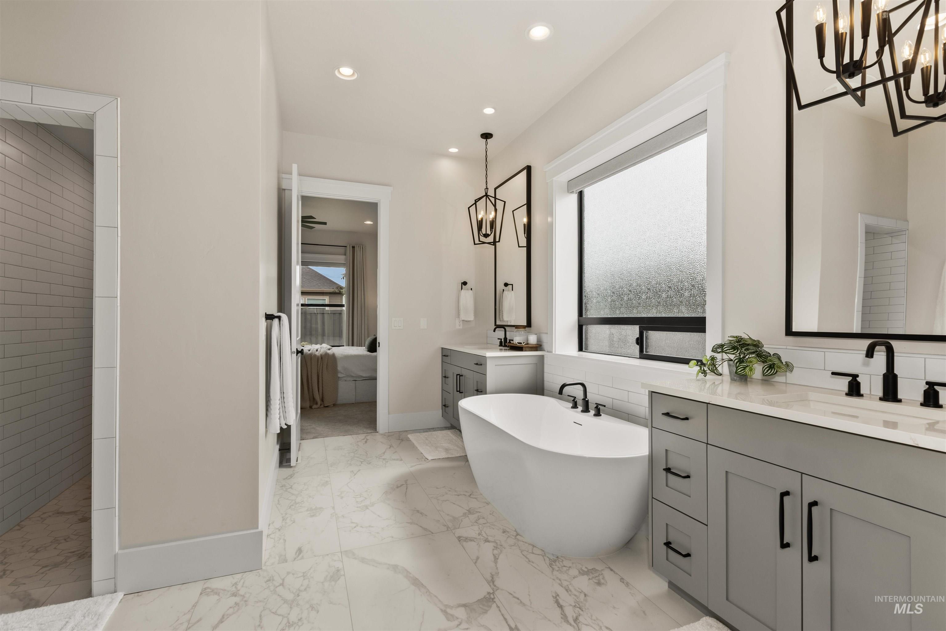 Bathroom featuring a chandelier, two vanities, a soaking tub, ensuite bath, and recessed lighting