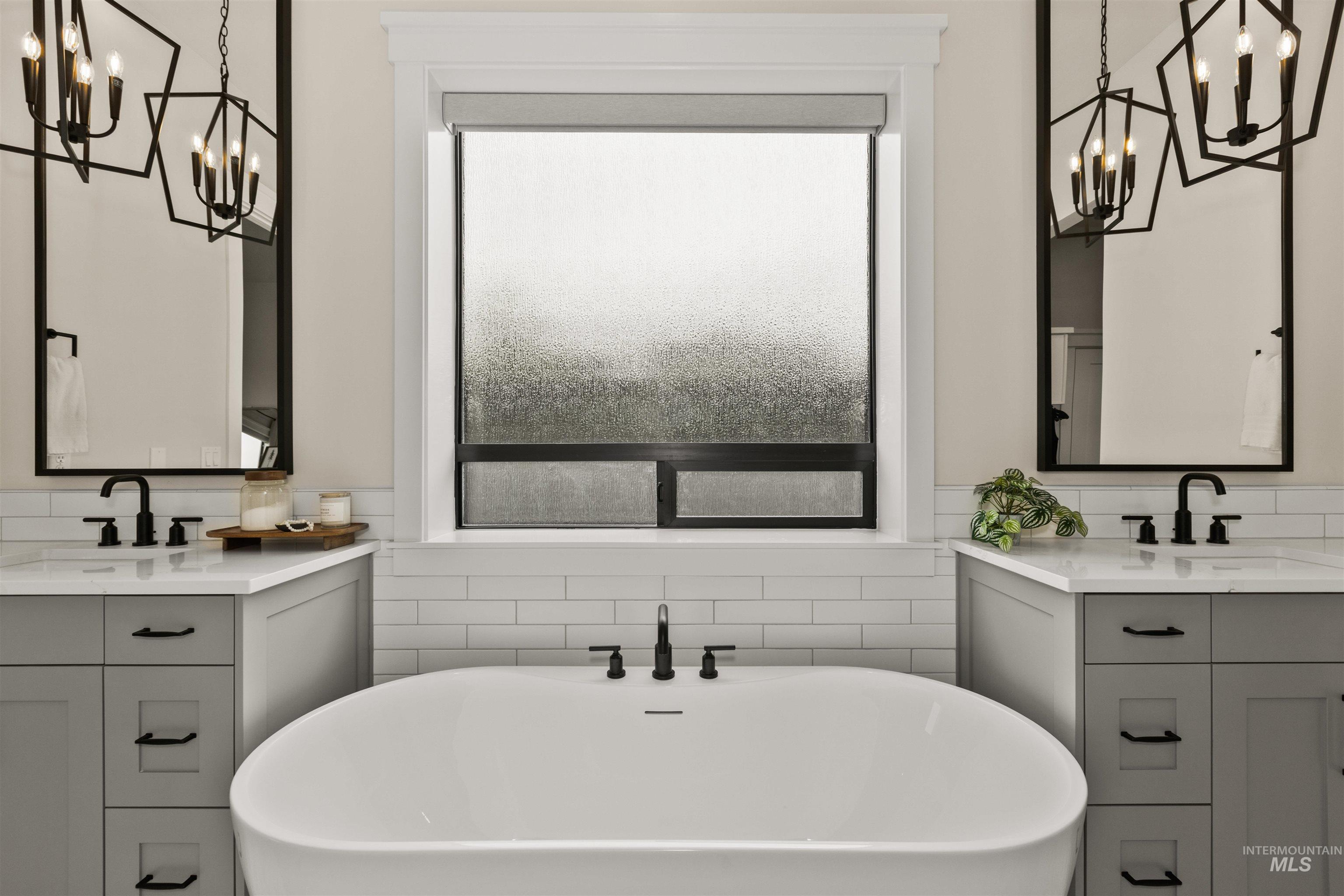 Bathroom featuring a chandelier, two vanities, and a freestanding bath
