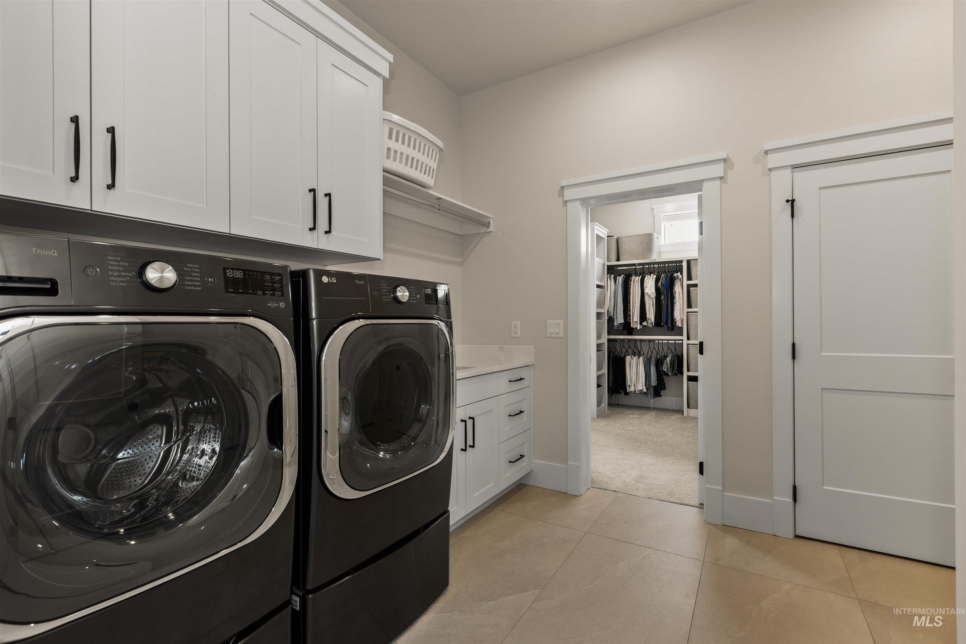 Laundry room featuring washing machine and dryer, cabinet space, and light tile patterned floors