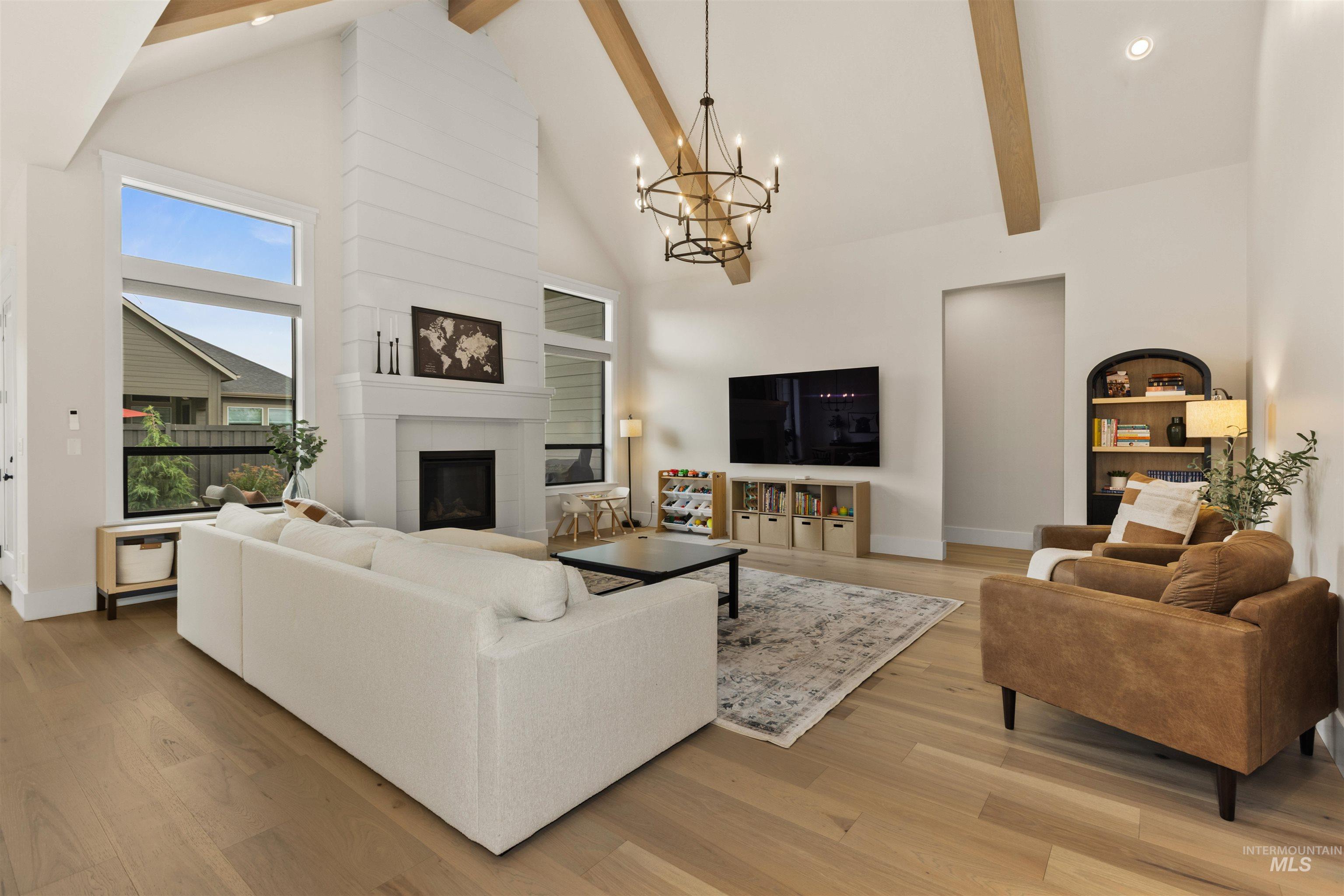 Living room featuring high vaulted ceiling, a chandelier, beamed ceiling, a tiled fireplace, and light wood-style floors