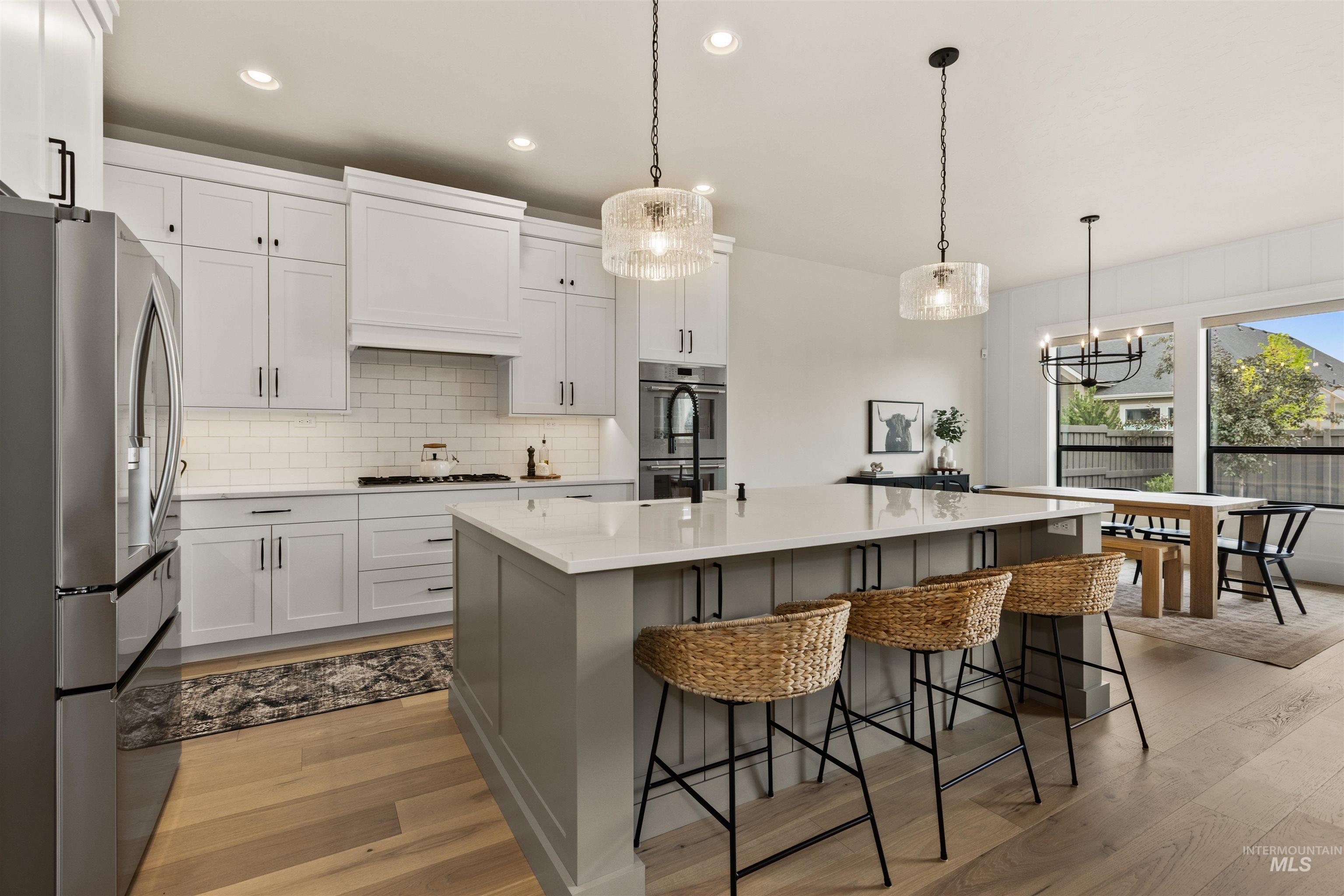 Kitchen with appliances with stainless steel finishes, custom range hood, light wood finished floors, a chandelier, and decorative backsplash