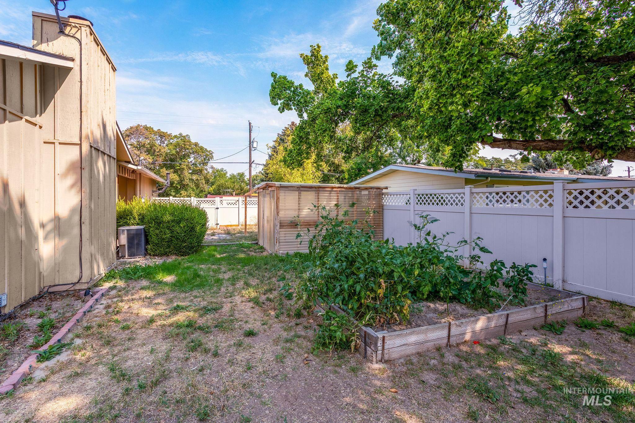 Fenced backyard featuring a vegetable garden and an outdoor structure