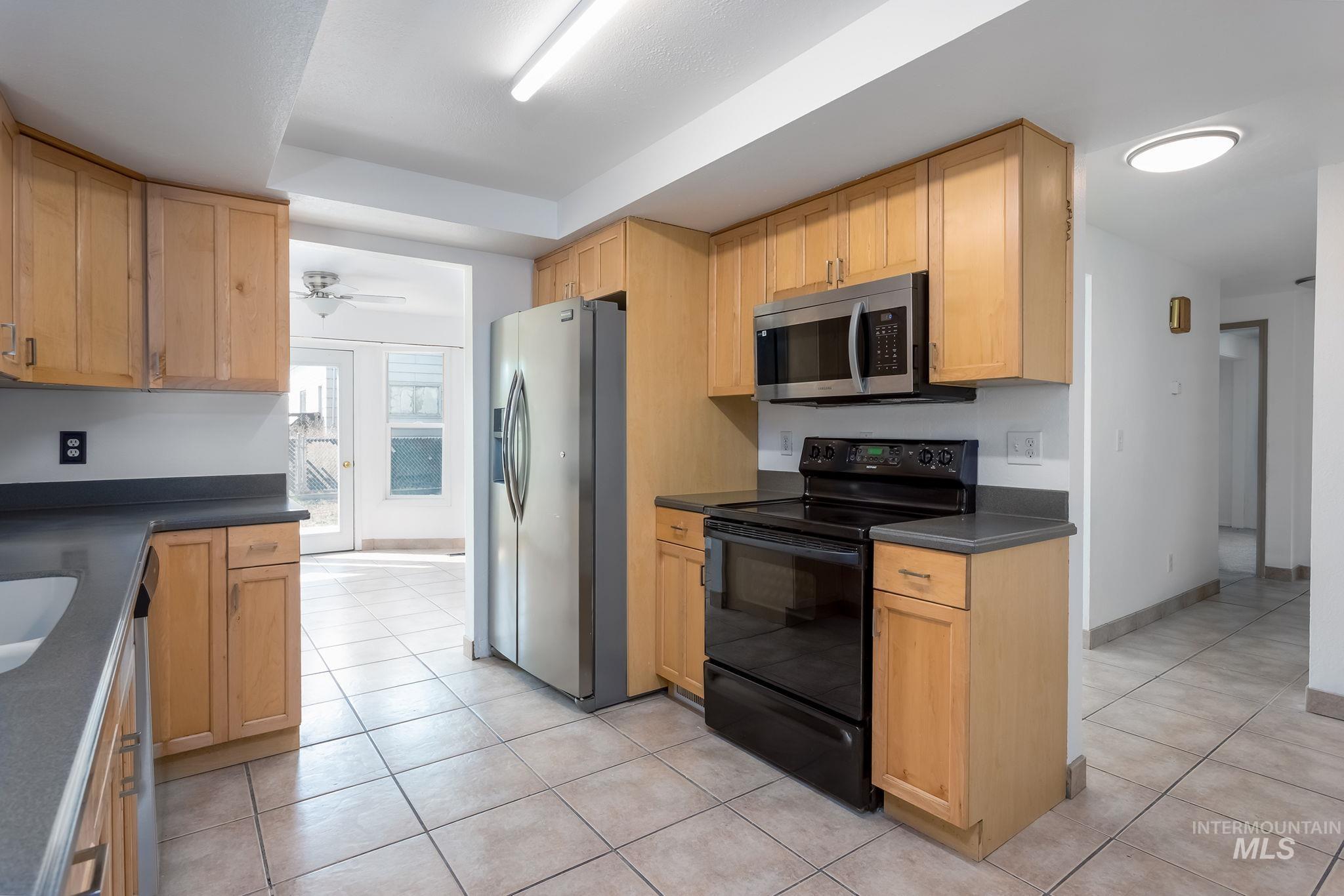 Kitchen with stainless steel appliances, dark countertops, light tile patterned flooring, and a ceiling fan