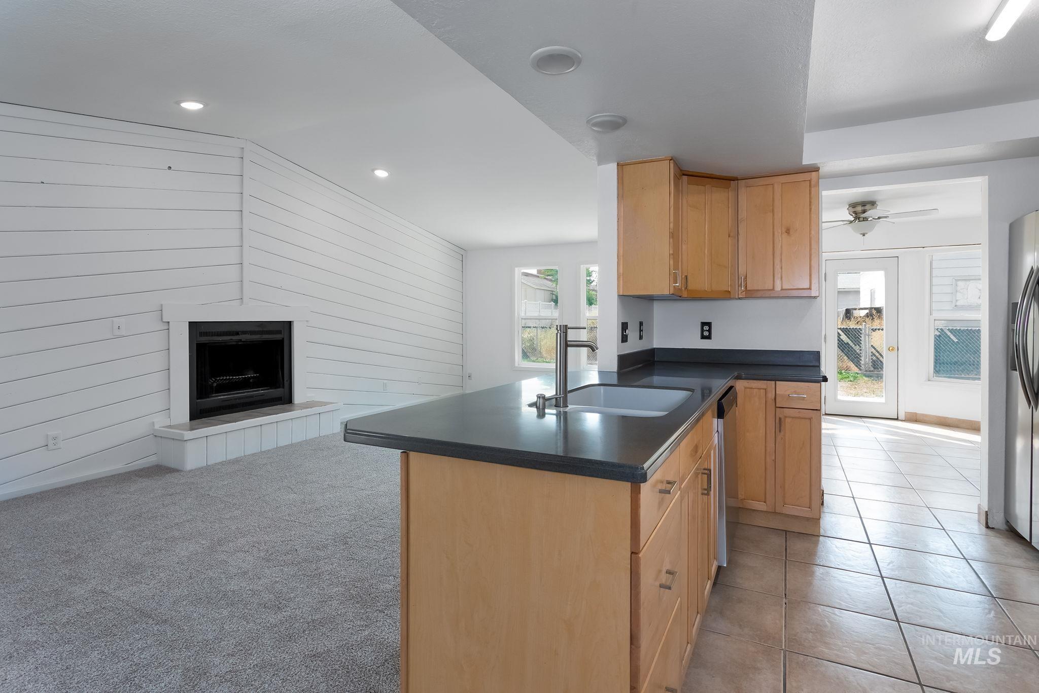 Kitchen with a peninsula, wood walls, dark countertops, ceiling fan, and open floor plan