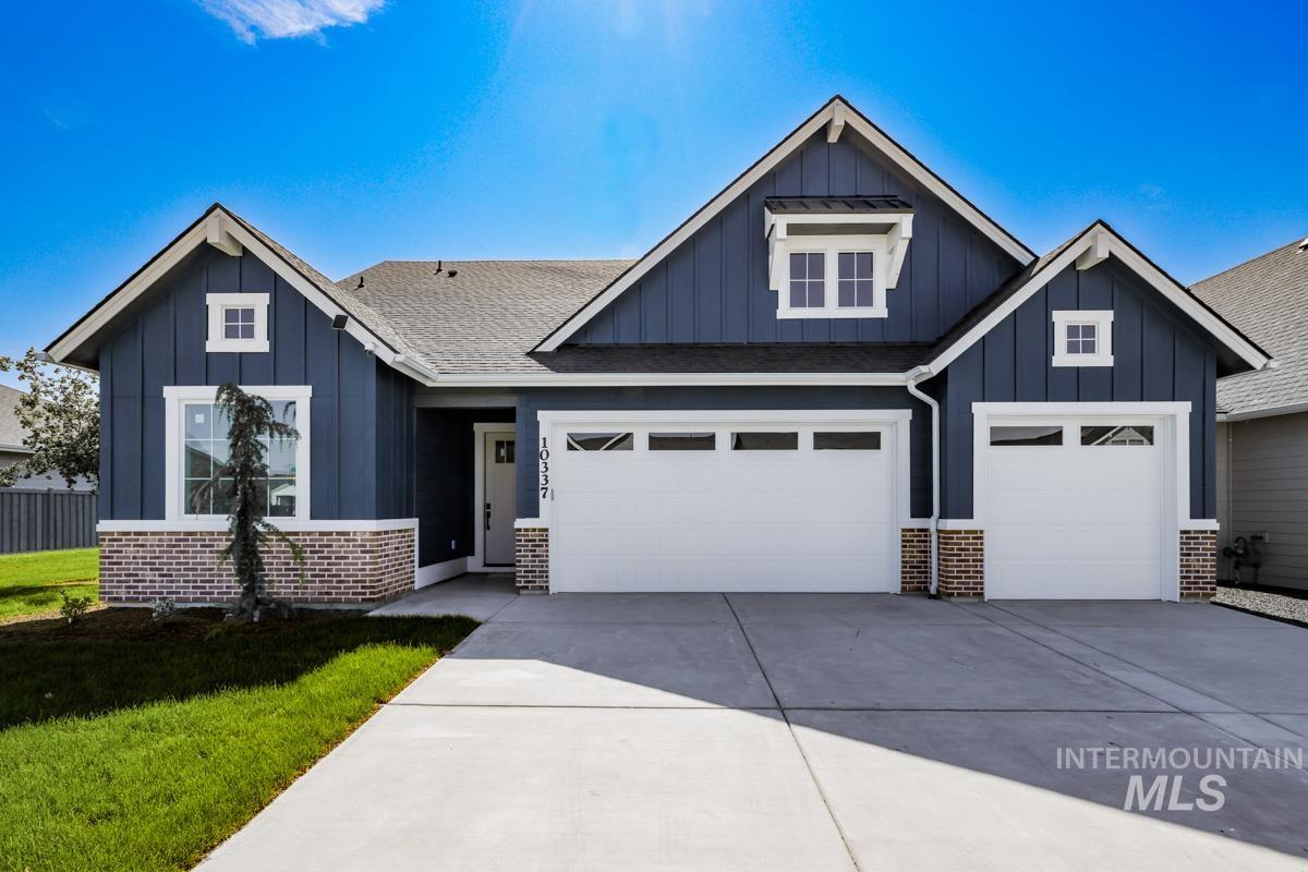 View of front facade featuring board and batten siding, brick siding, driveway, and a front yard
