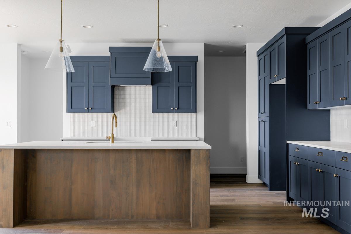 Kitchen with backsplash, hanging light fixtures, dark wood-style flooring, blue cabinets, and recessed lighting