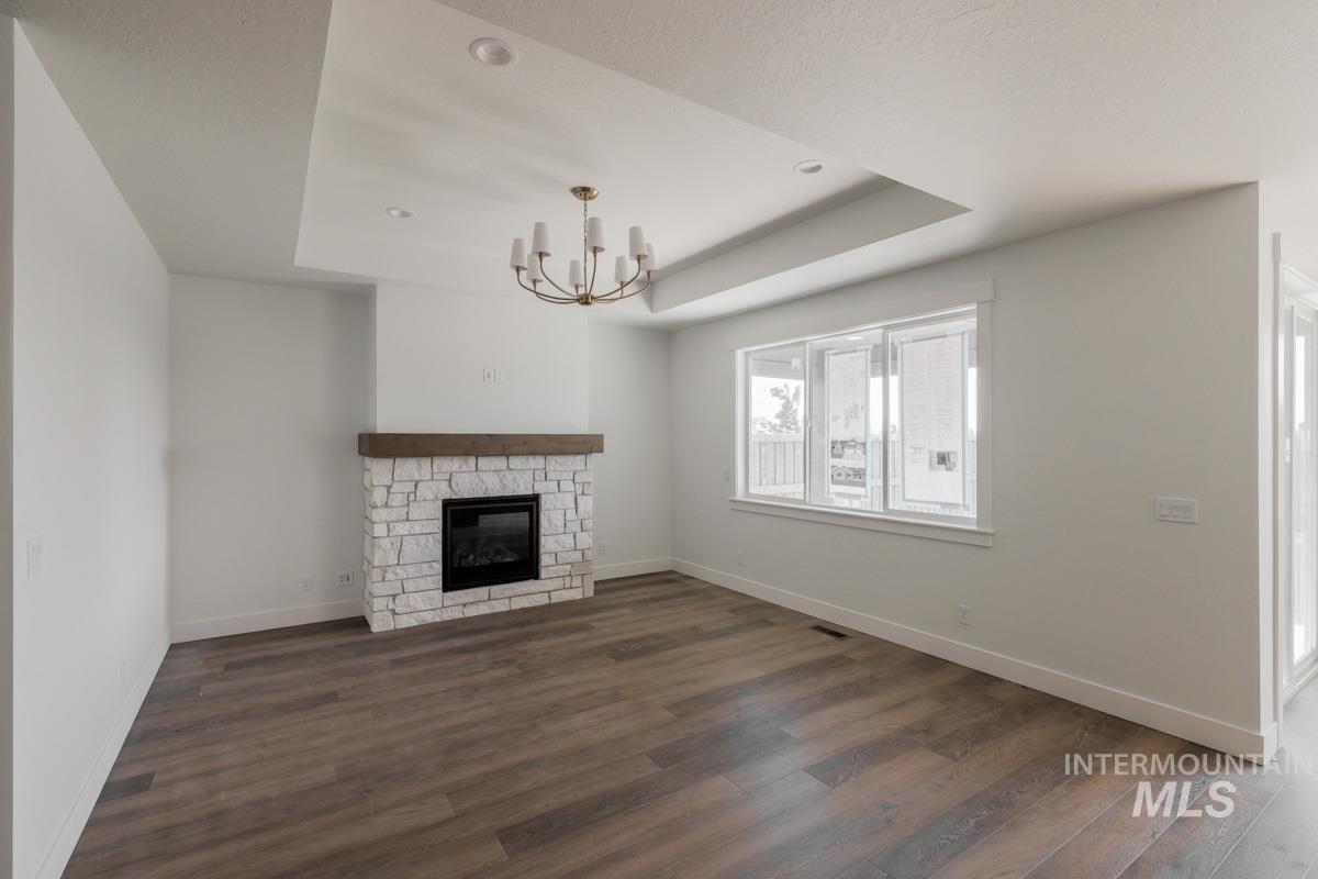 Unfurnished living room with a tray ceiling, dark wood-style flooring, a stone fireplace, and a chandelier