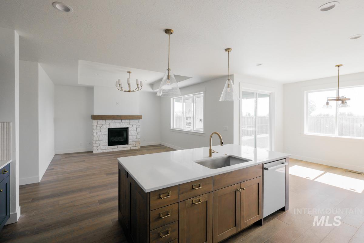 Kitchen with a chandelier, open floor plan, a stone fireplace, hanging light fixtures, and dark wood-style floors